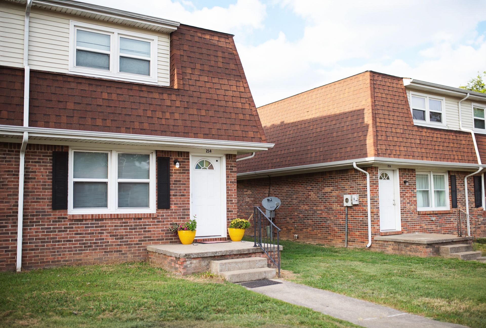 Two brick houses with white trim and black shutters are next to each other.
