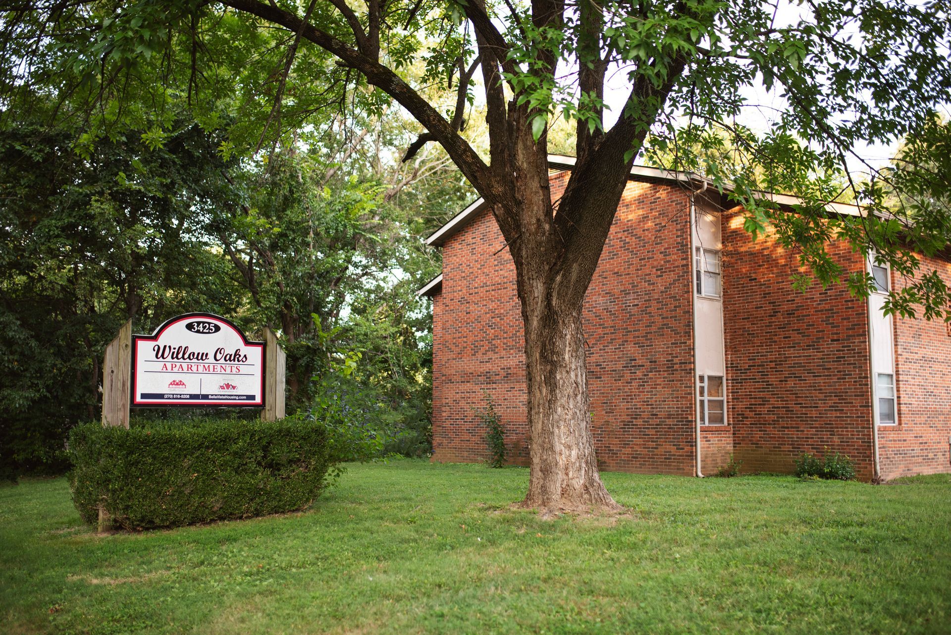 A brick building with a sign in front of it and a tree in front of it.