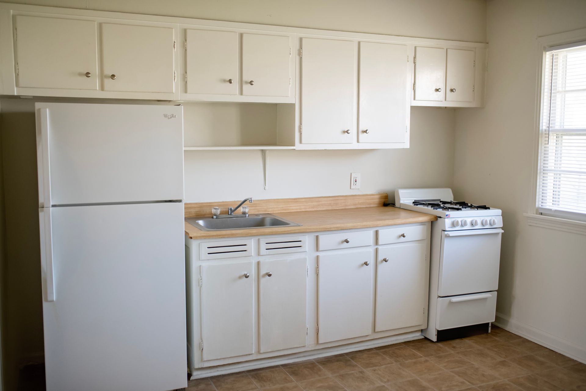 An empty kitchen with white cabinets , a refrigerator , stove and sink.