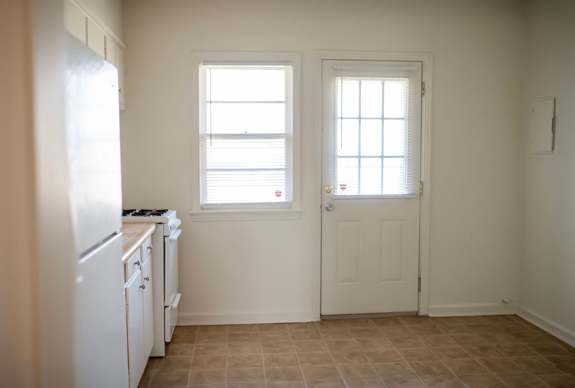 An empty kitchen with white cabinets , a refrigerator , a stove , and a door.