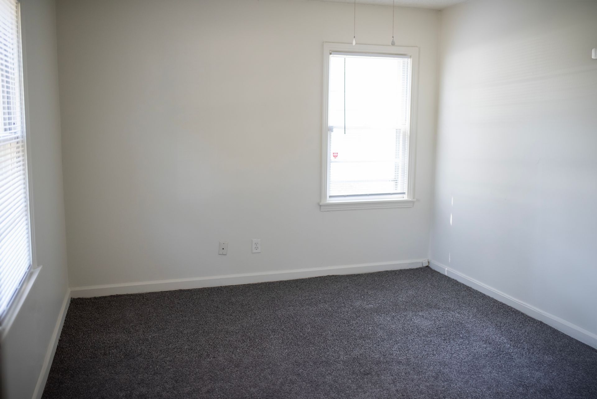 An empty bedroom with a window and a carpeted floor.