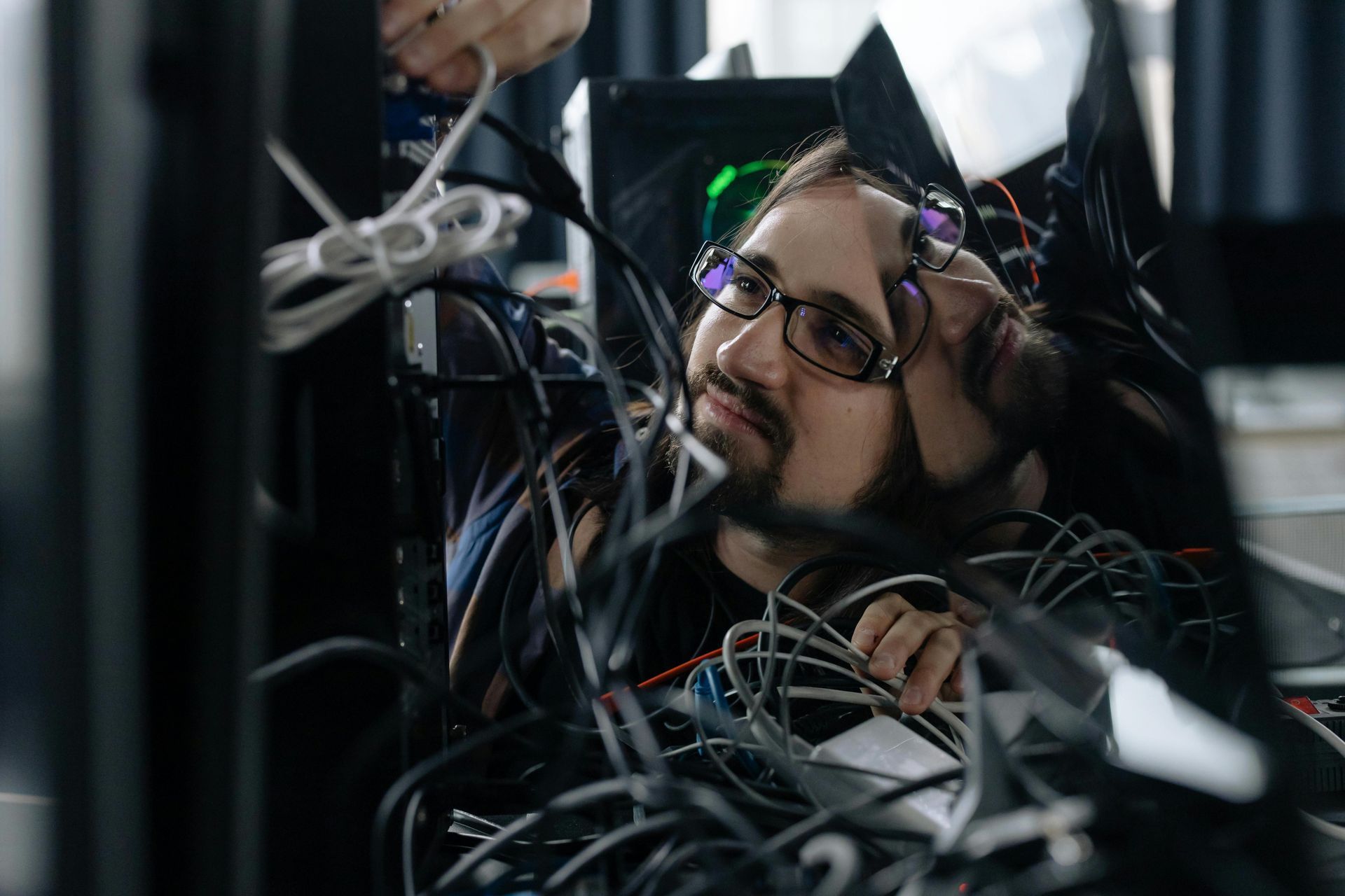 Man with glasses looks up, surrounded by tangled cables and equipment.