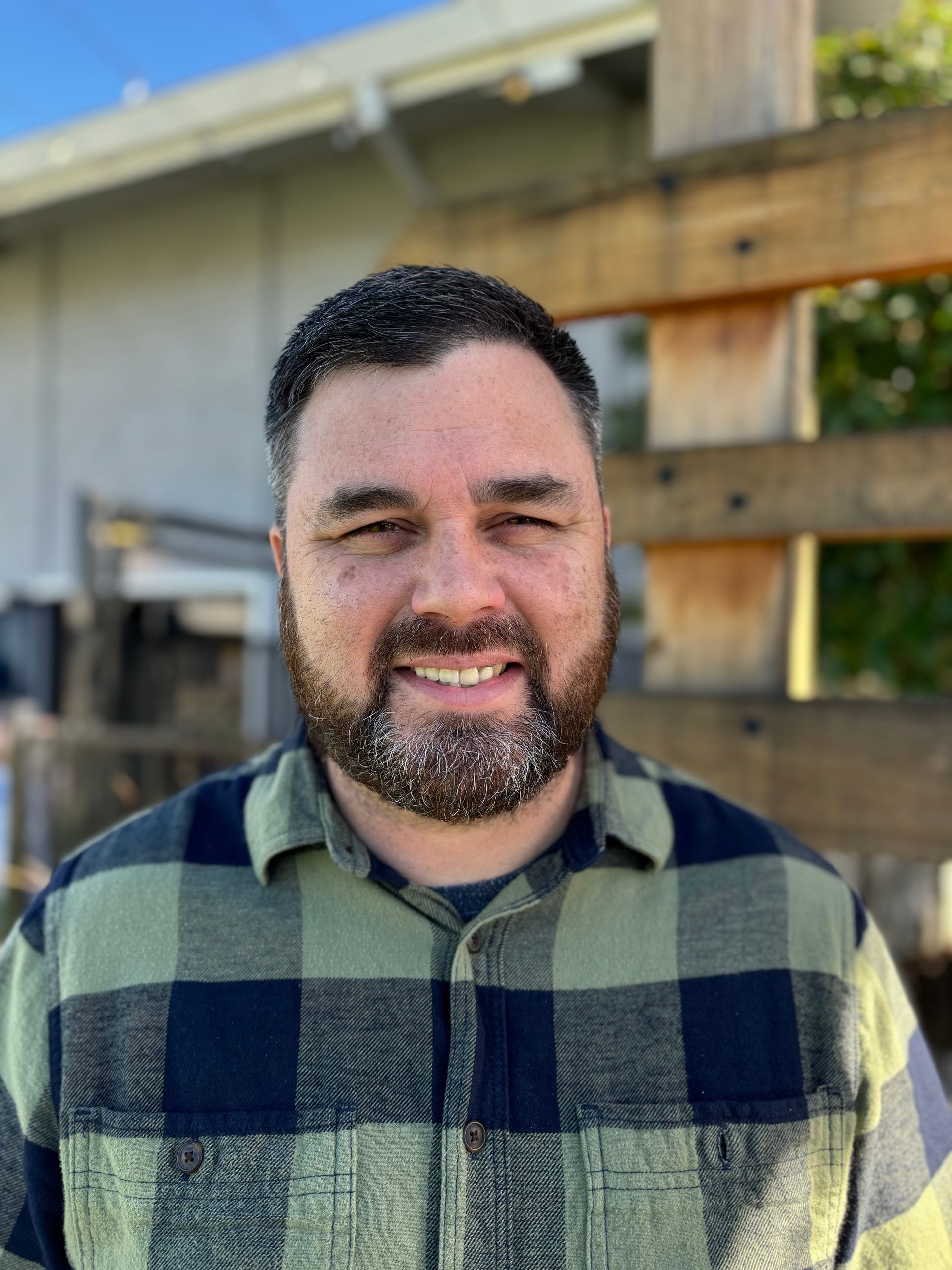 A man with a beard is wearing a plaid shirt and smiling.