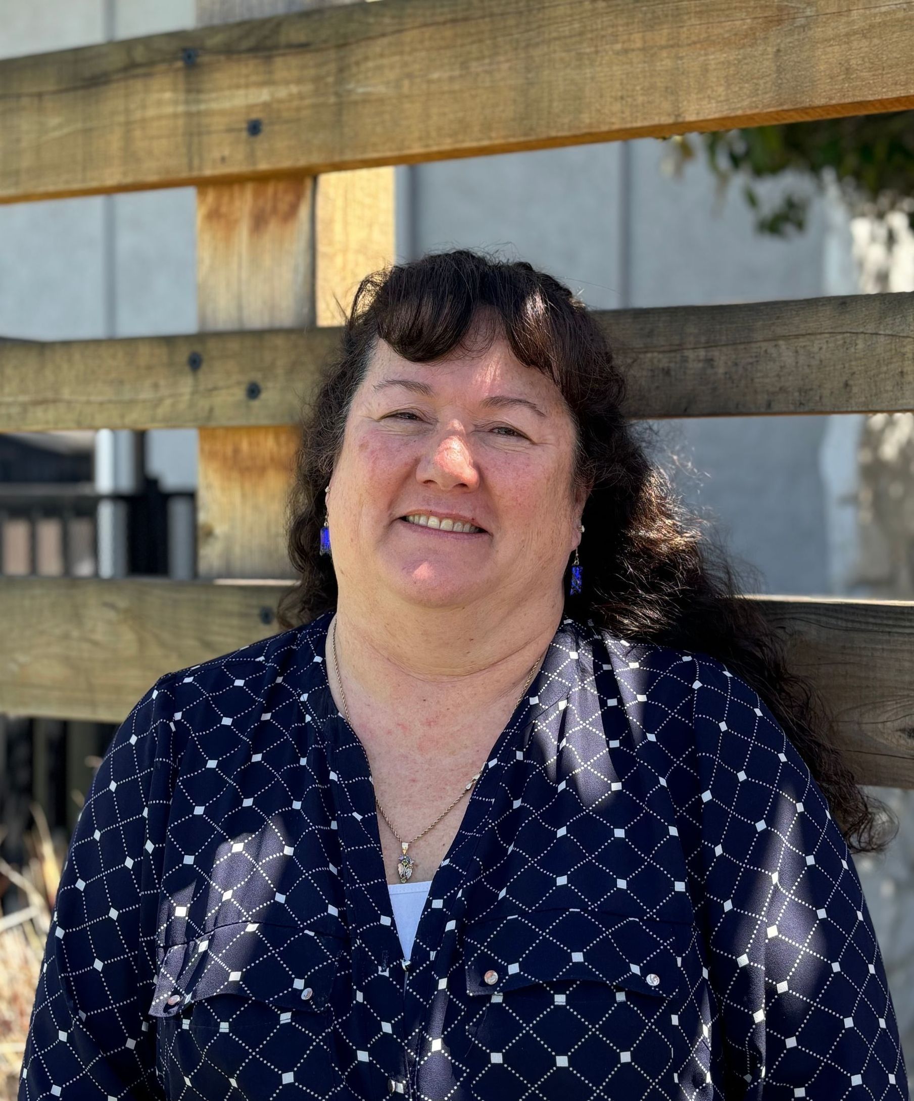 A woman in a blue shirt is standing in front of a wooden fence.