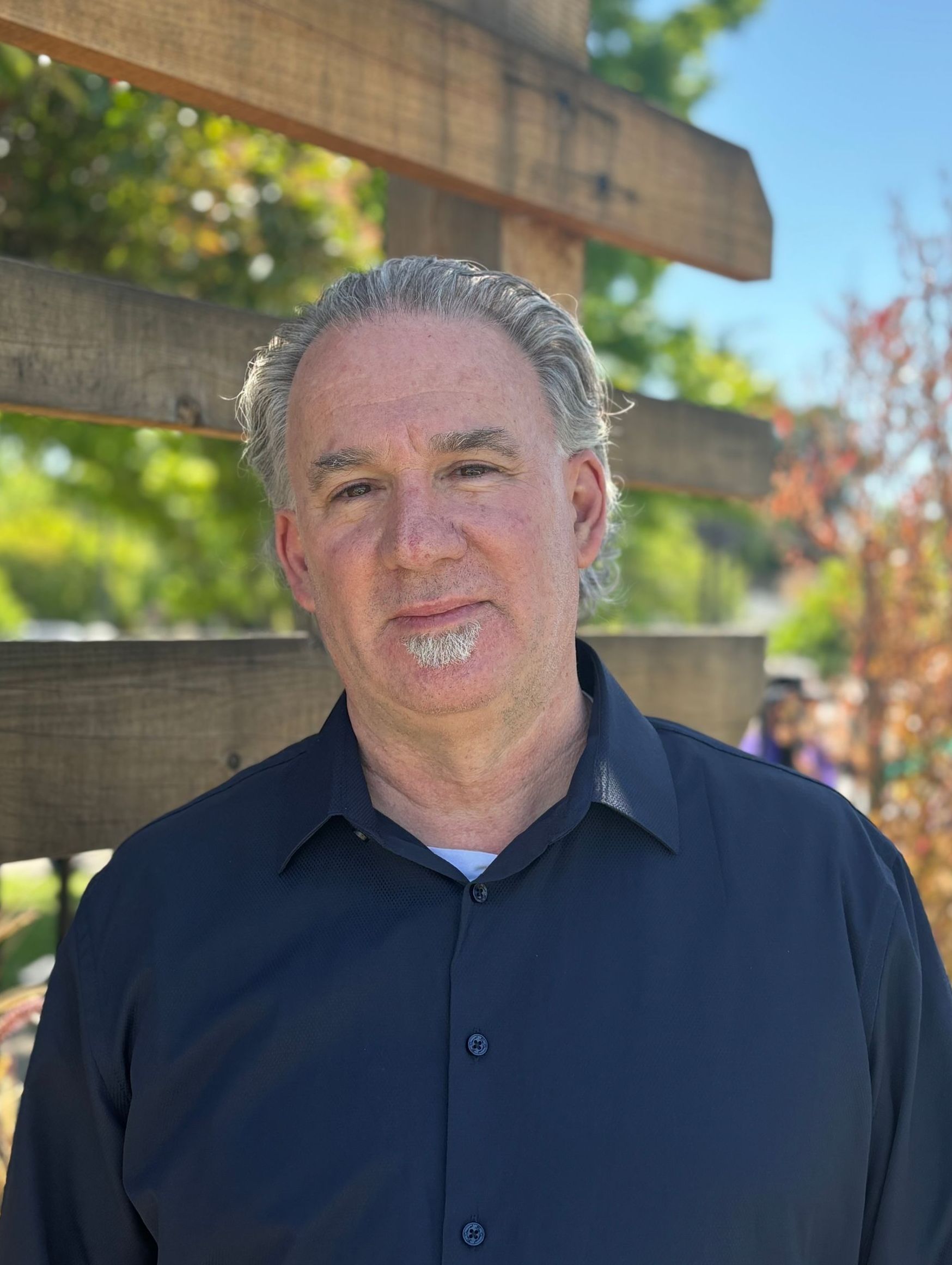 A man in a black shirt is standing in front of a wooden fence.