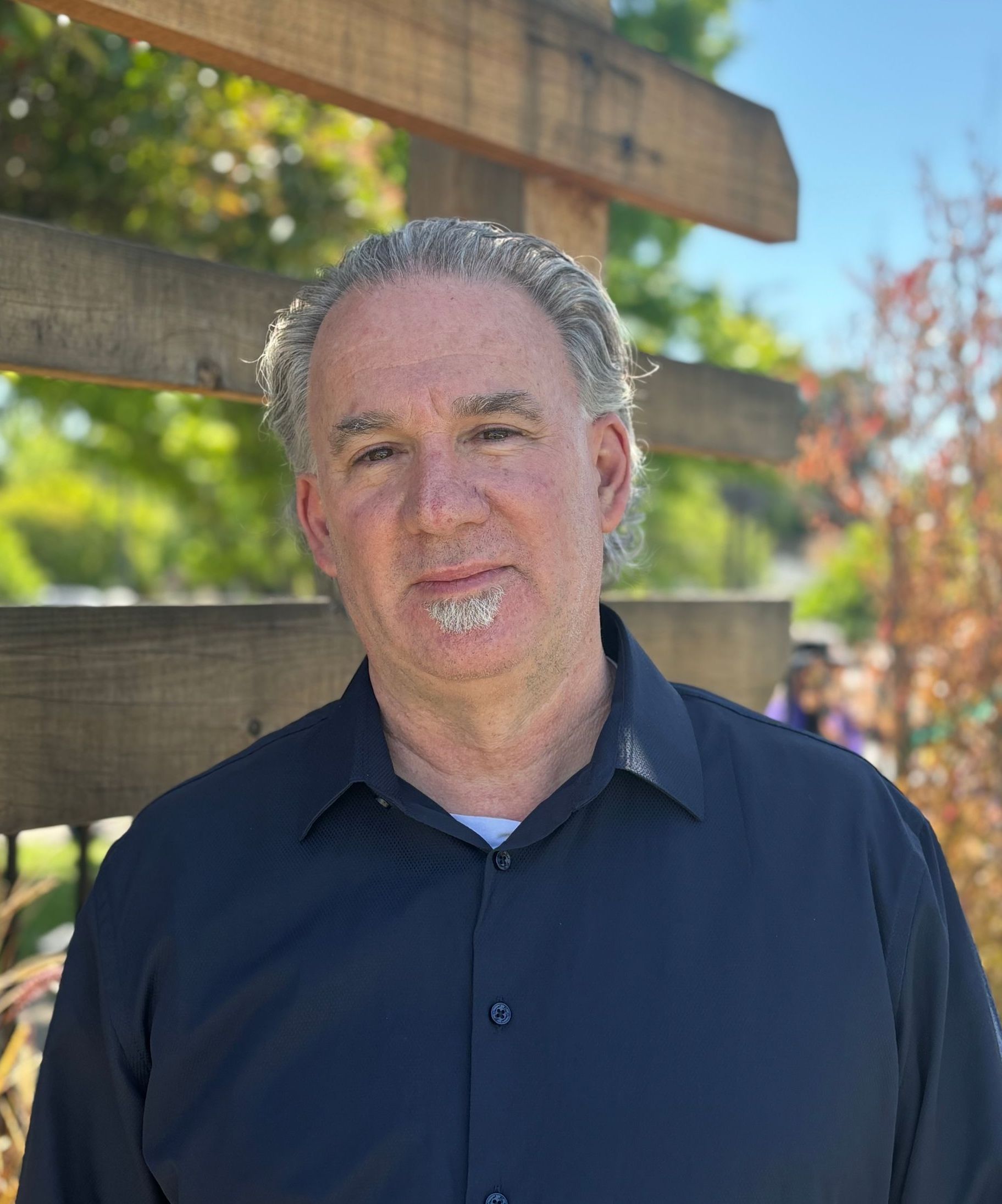 A man in a black shirt is standing in front of a wooden fence.