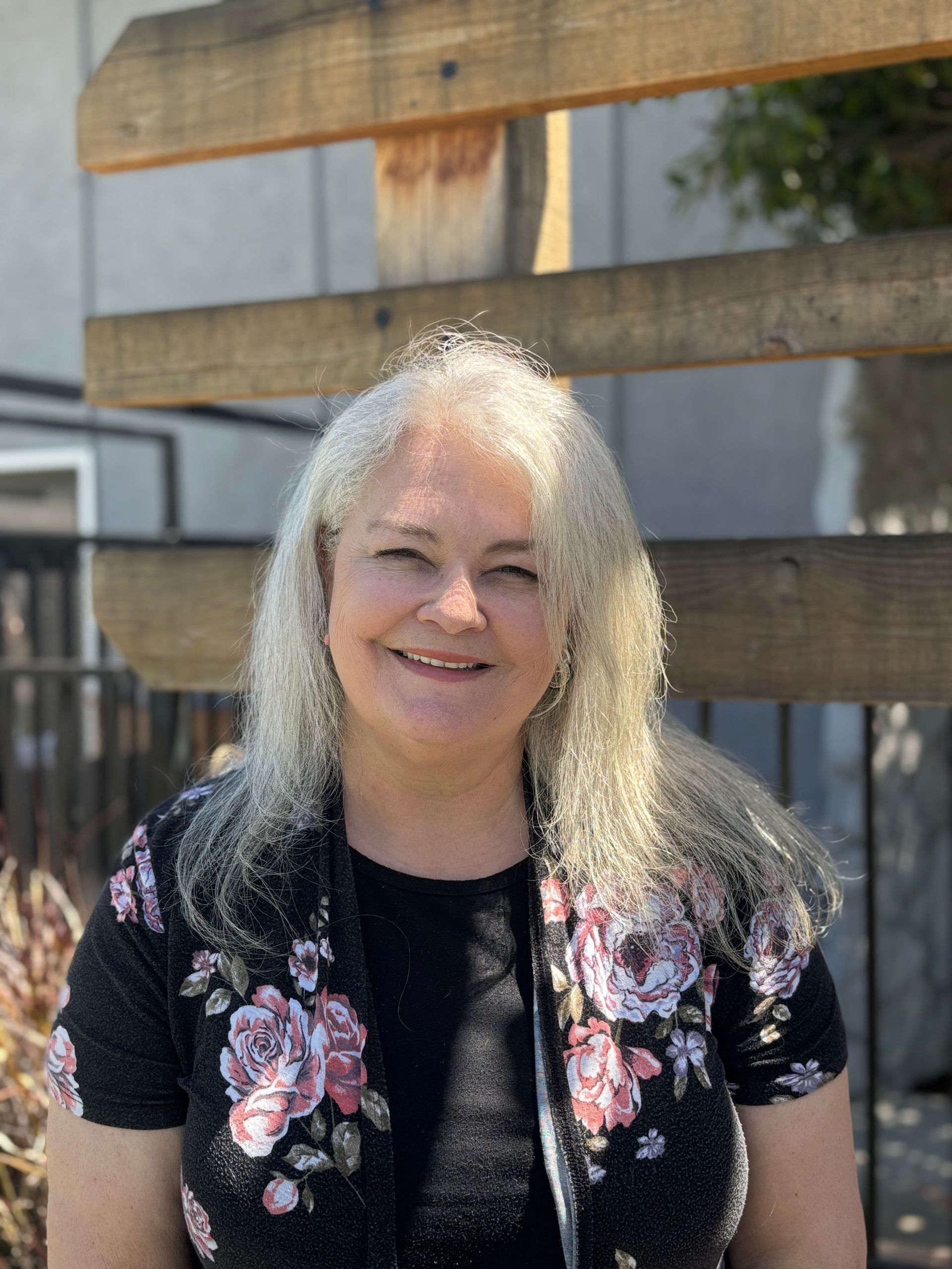 A woman wearing a black shirt and a floral jacket is smiling for the camera.