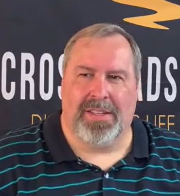 A man with a beard is wearing a striped shirt and smiling.