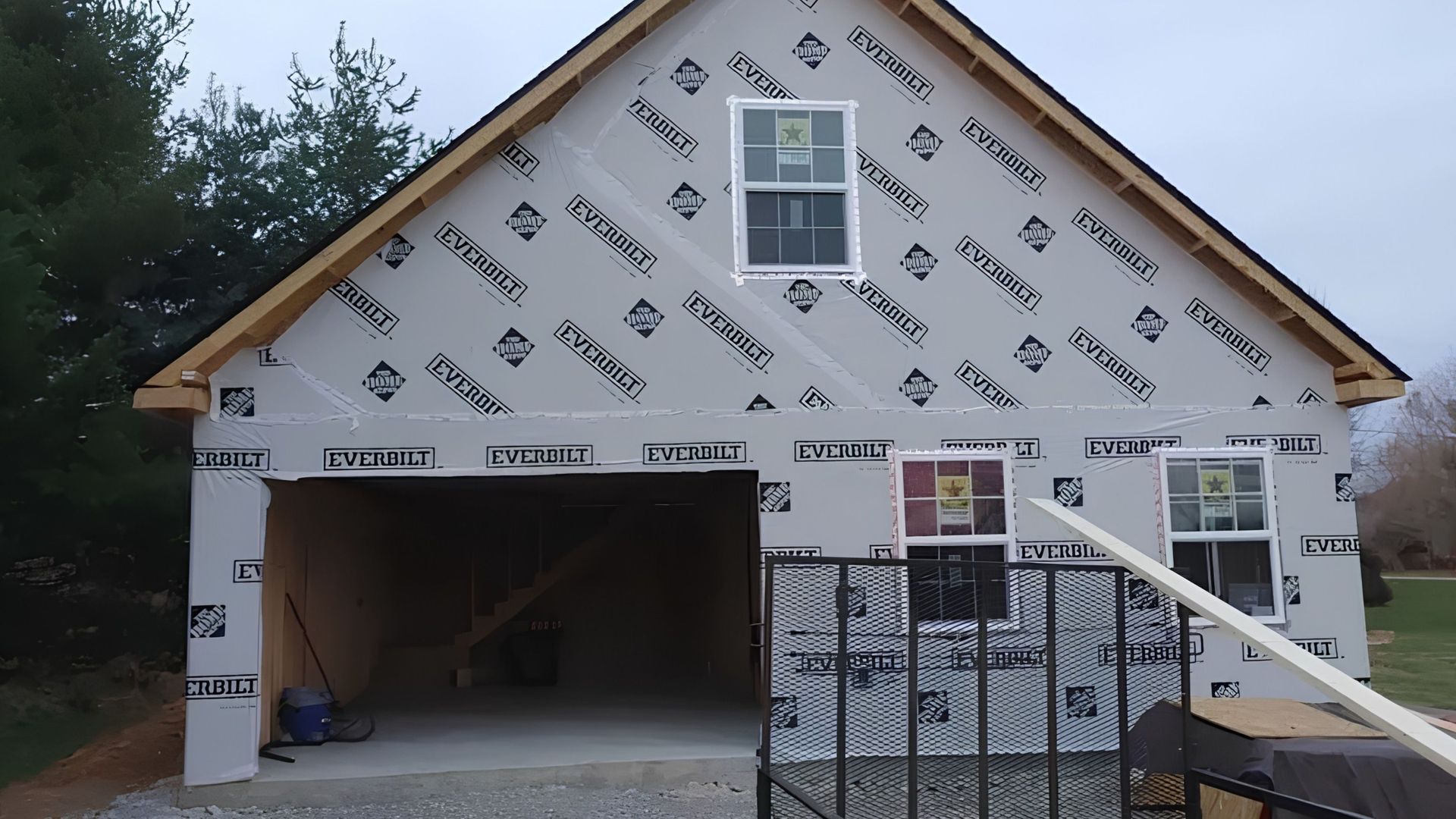 House under construction wrapped in white house wrap, with open garage and front steps.