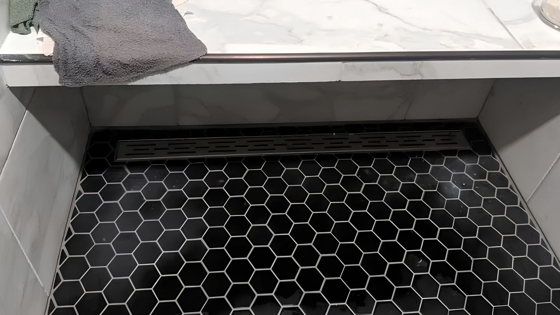 Hexagonal black tile floor beneath a white ledge with a gray cement patch on the left corner.
