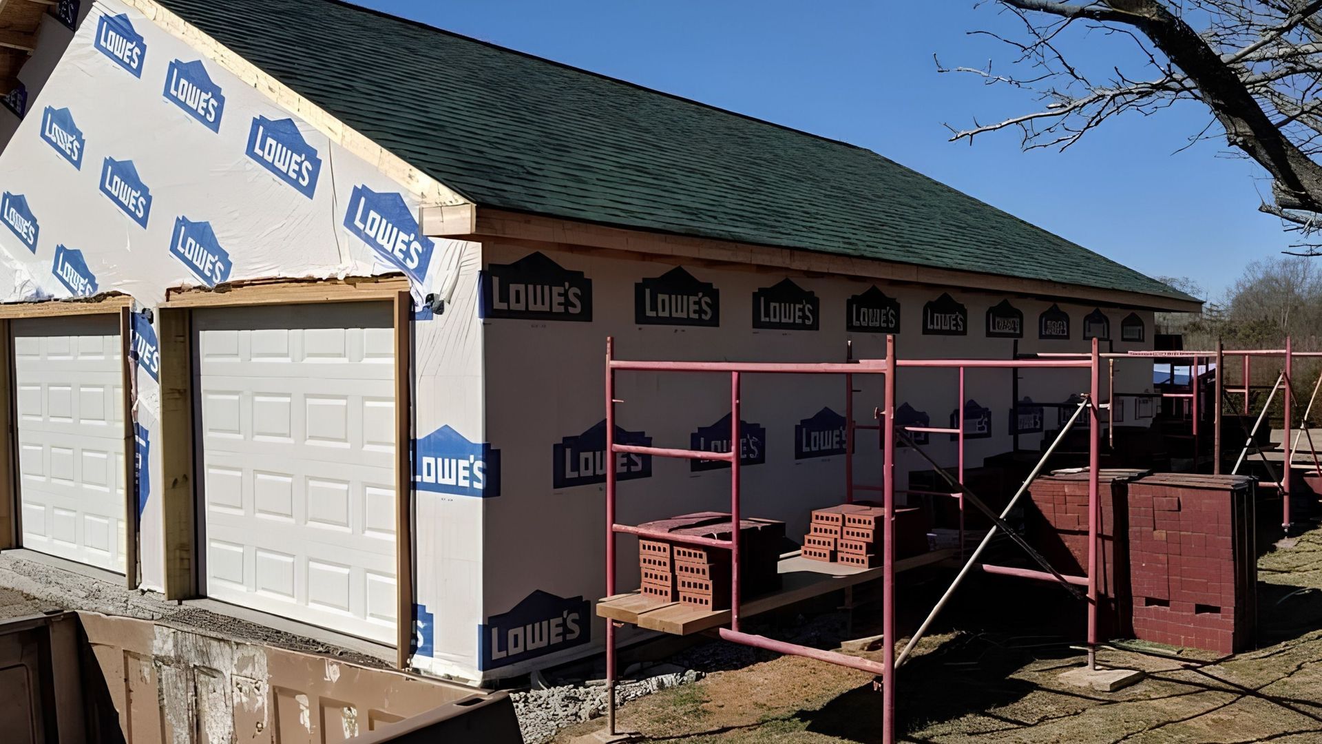 House under construction with green roof, siding, and pink scaffolding against a blue sky