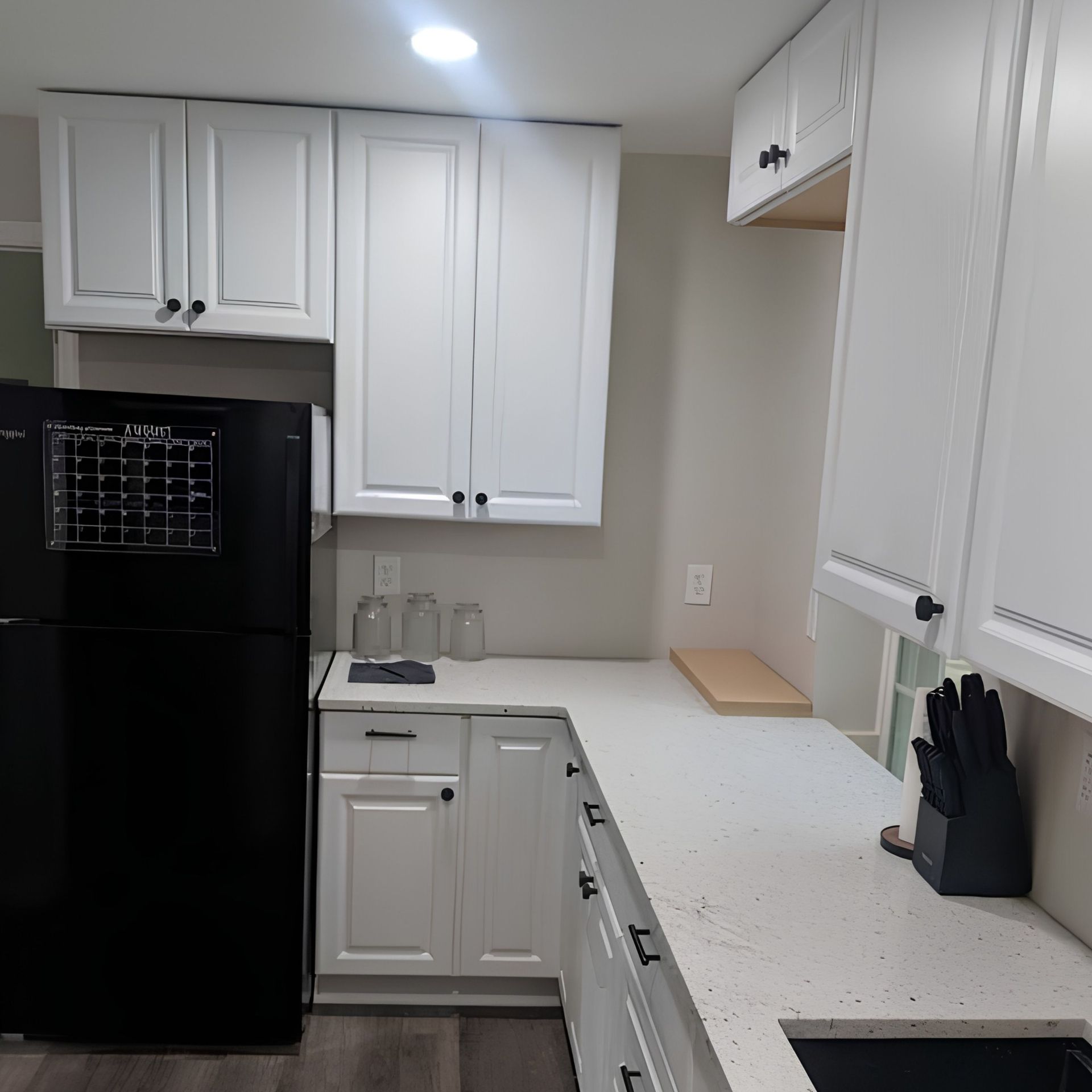 Compact white kitchen with black refrigerator, white cabinets, and speckled countertop.