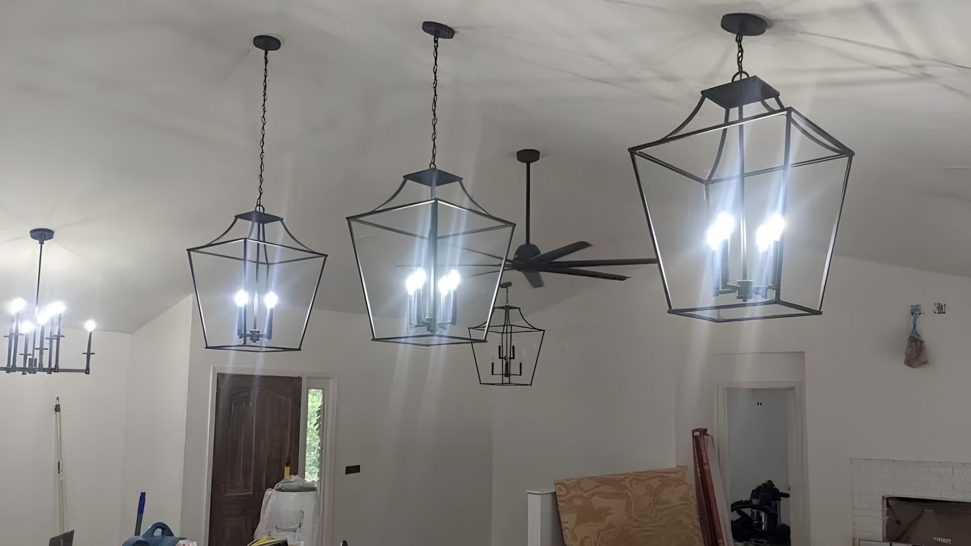 Ceiling with three hanging geometric lanterns lit in a living room, with a ceiling fan and wall decor.