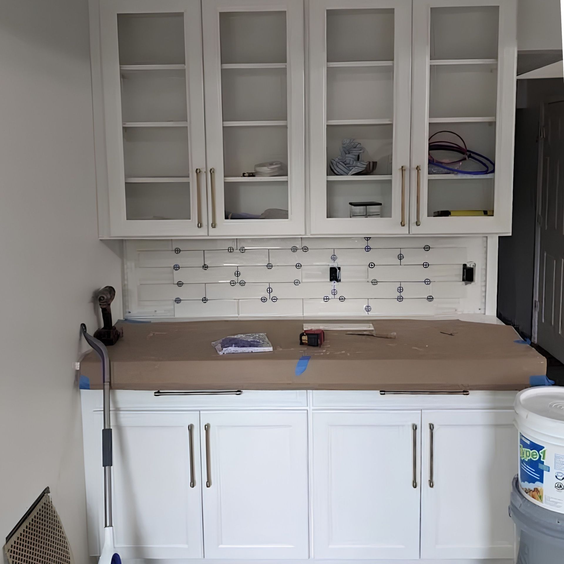 White kitchen cabinets and a countertop under renovation, with tools and supplies on the counter.