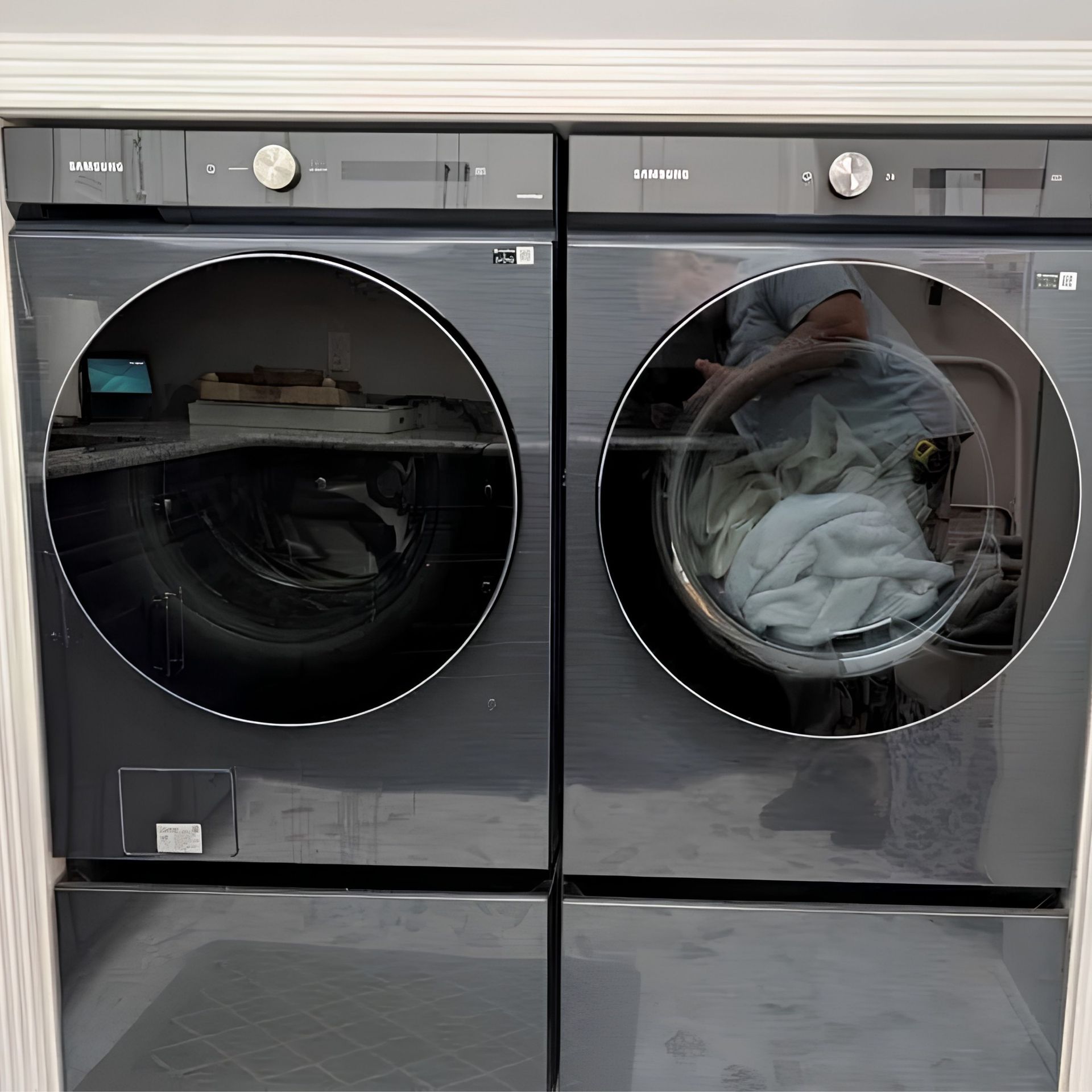 Two gray front-loading washers with circular doors; one has clothes visible inside.
