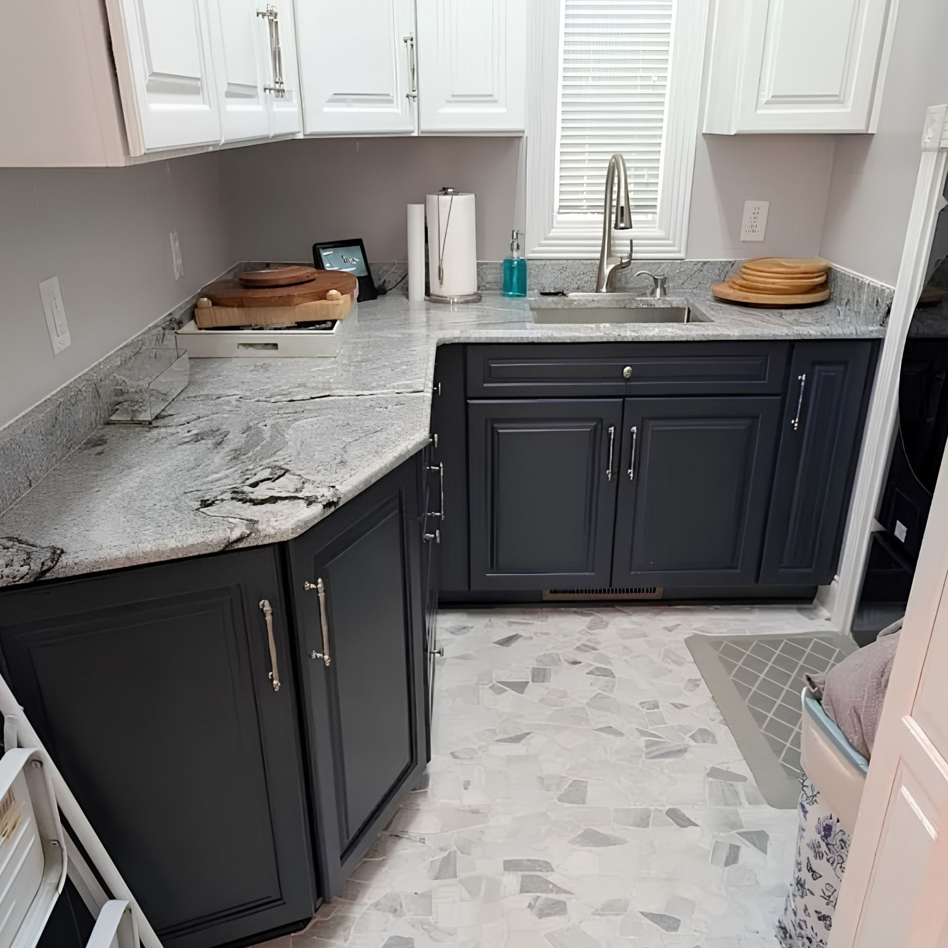 Compact kitchen with black cabinets, white granite counters, and a stainless sink under white upper cabinets.