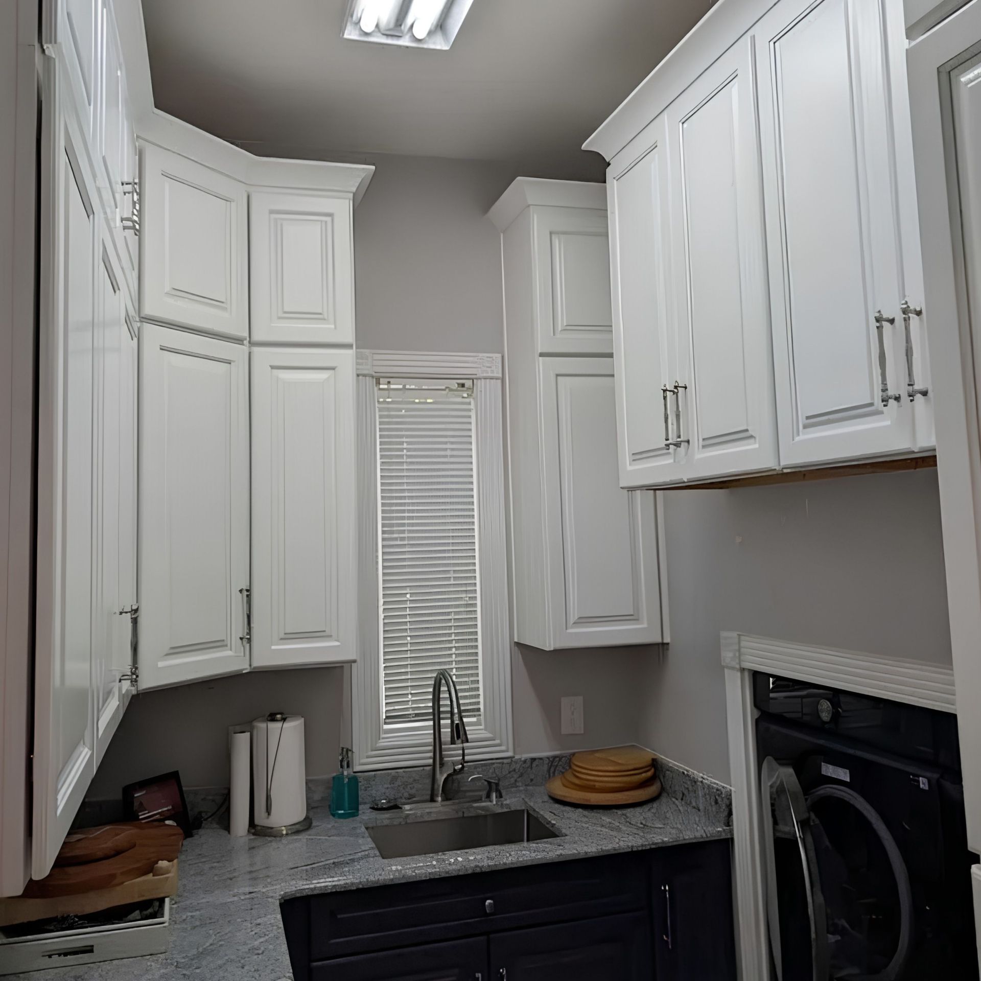 Small laundry room with white cabinets, granite countertop, sink, and stacked washer and dryer.