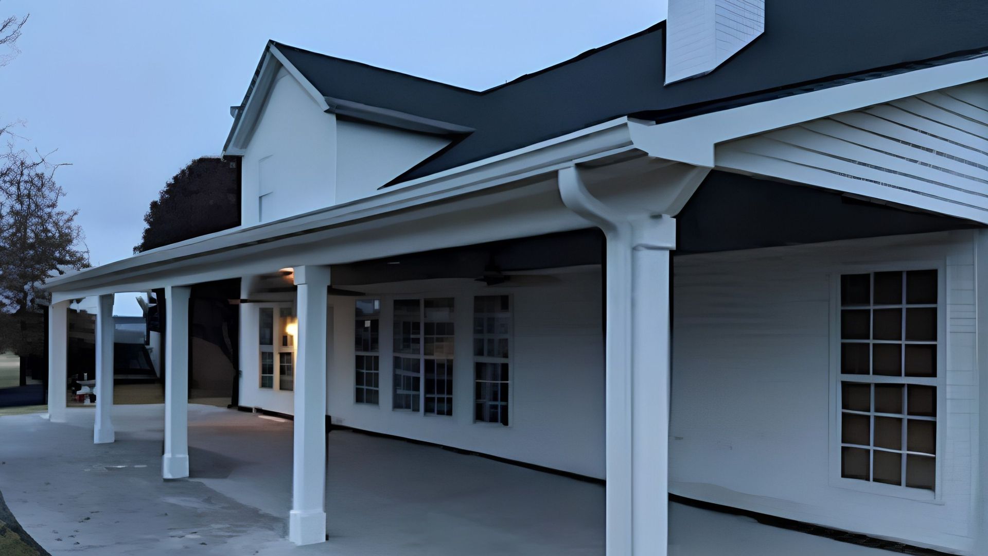 White building with covered porch, columns, and multi-pane windows at dusk