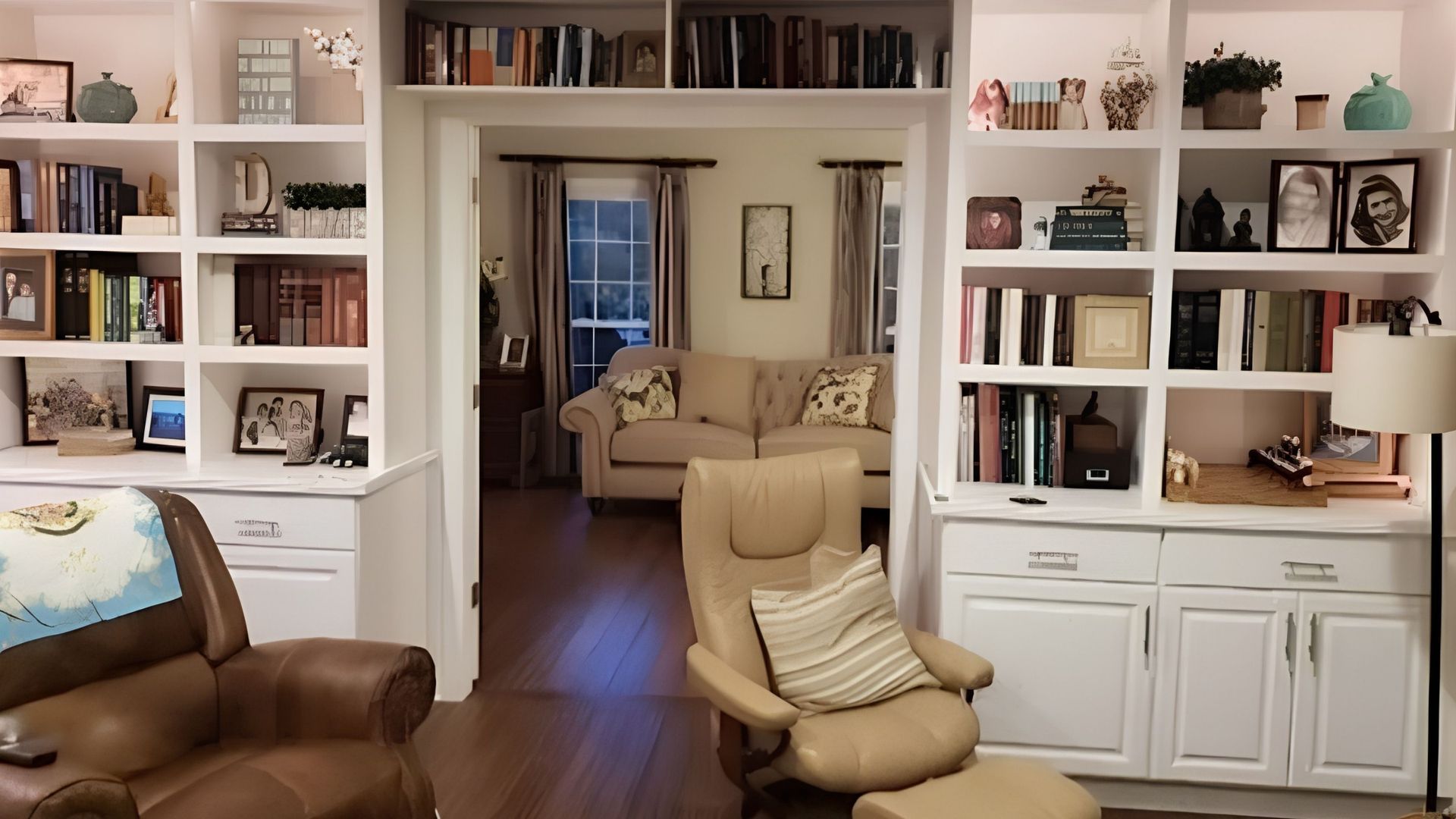 Bright living room with built-in bookshelves, fireplace, leather chair, and beige armchair facing a doorway