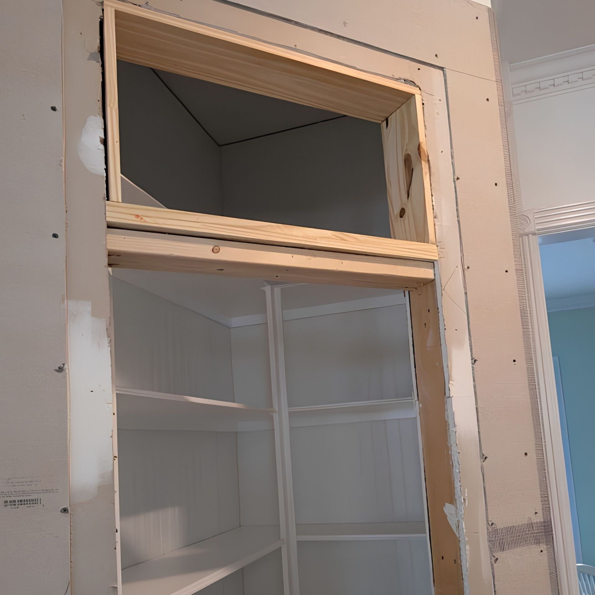 Partially finished doorway with exposed framing above a white built-in shelving cabinet