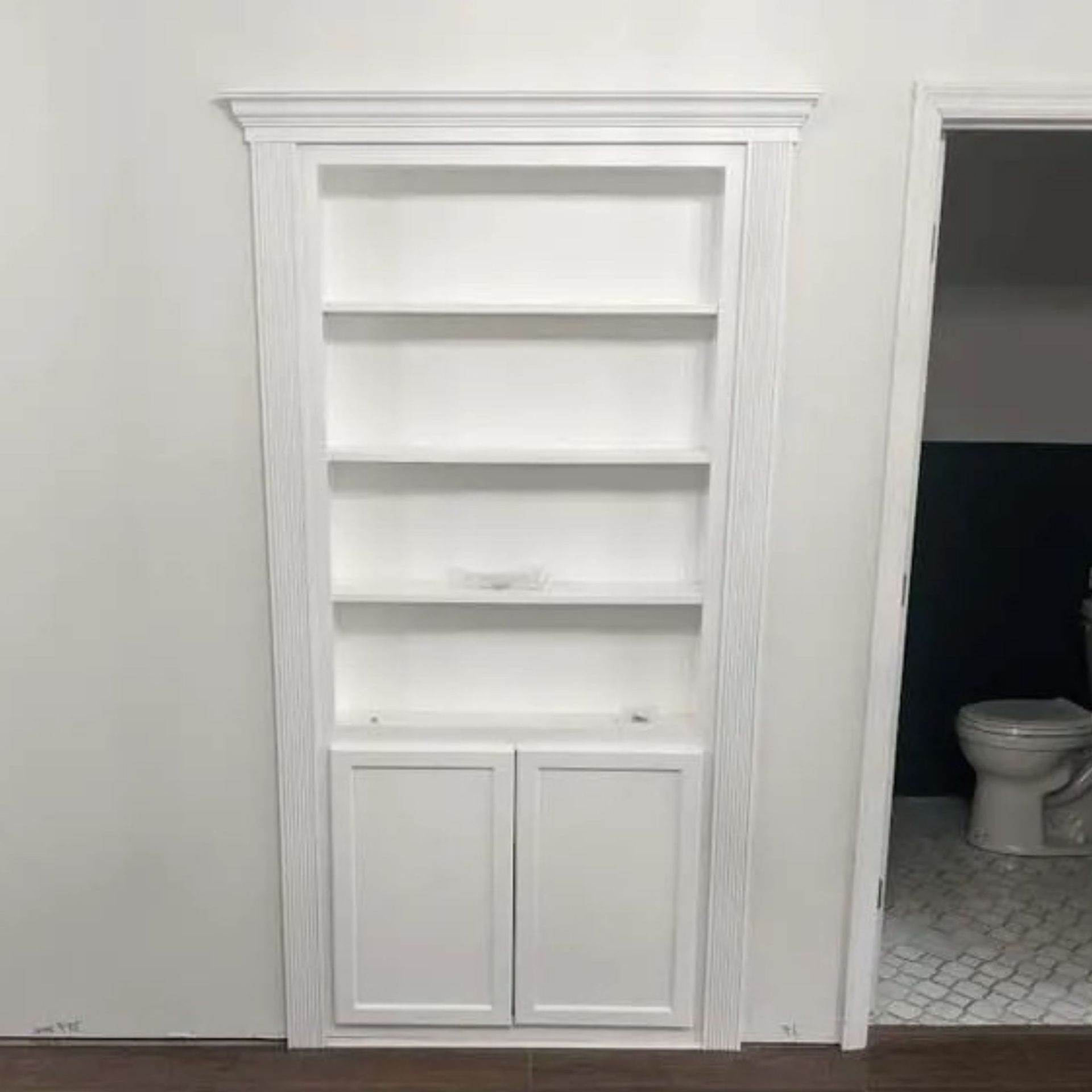 Built-in white bathroom shelves beside an open doorway to a toilet room