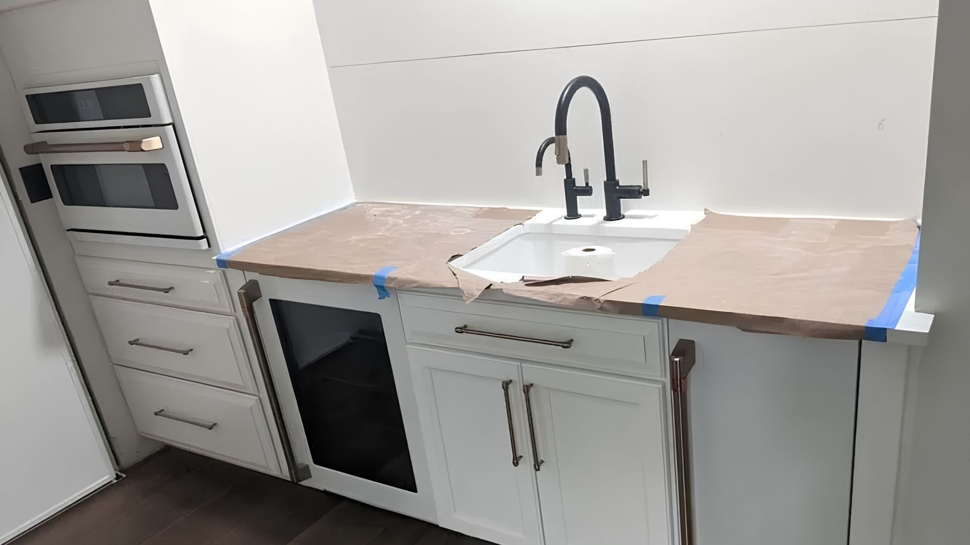 Modern kitchen countertop with sink, black faucet, white cabinets, and built-in oven on the left