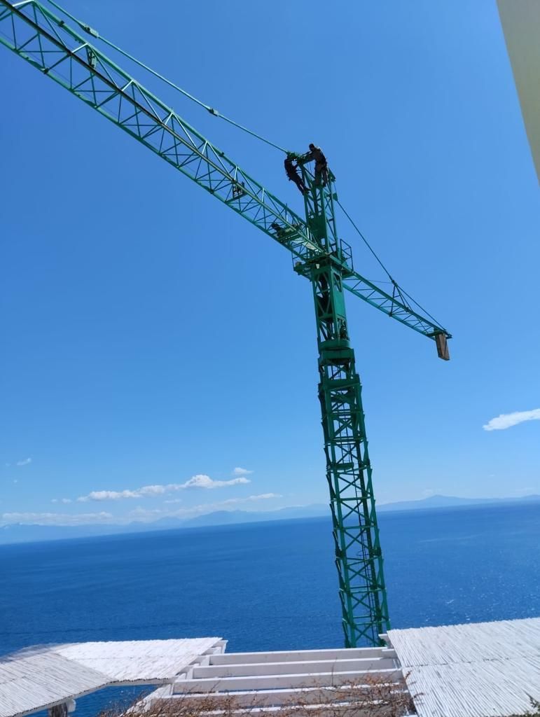 Una gru da costruzione verde si erge sopra un oceano blu sotto un cielo limpido, vista da una terrazza sul tetto.