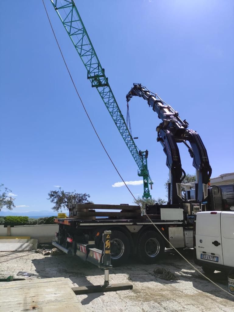 Una gru da costruzione solleva travi d'acciaio accanto a un camion sotto un cielo azzurro e limpido.