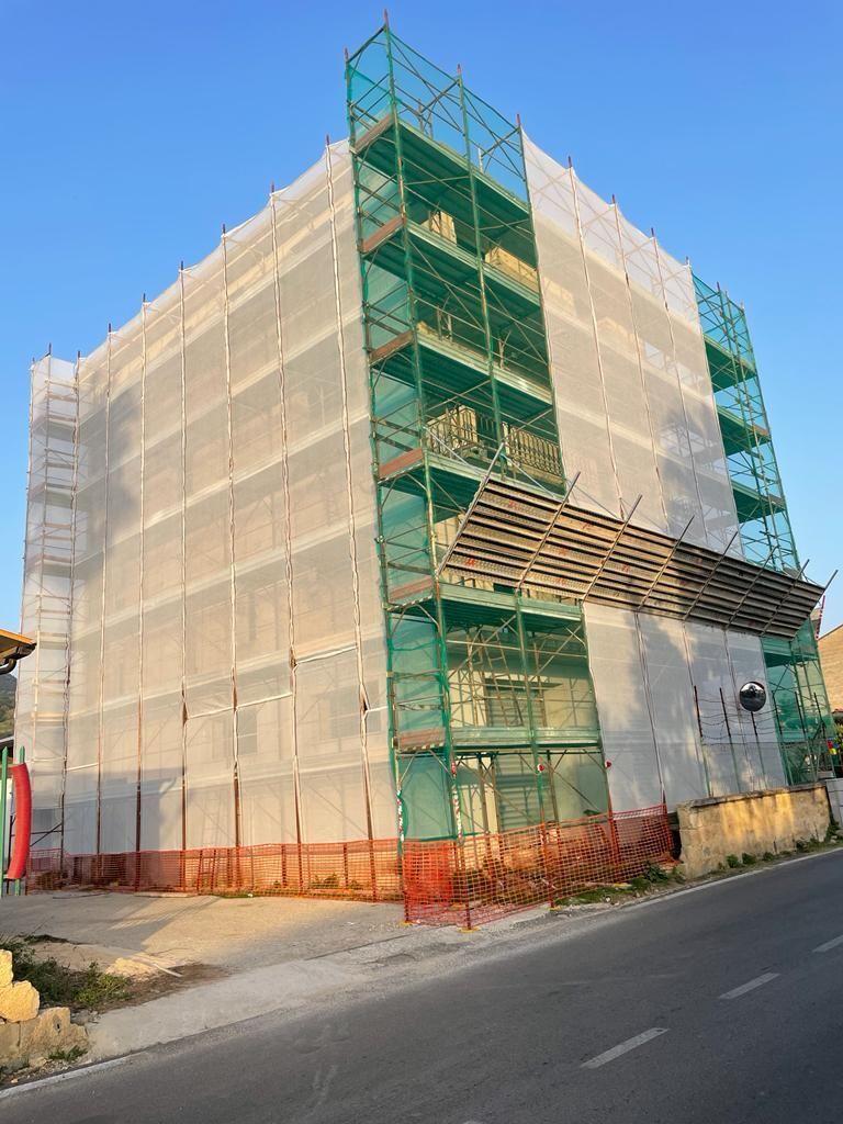 Impalcature e reti verdi coprono un edificio a più piani in costruzione a lato di una strada.
