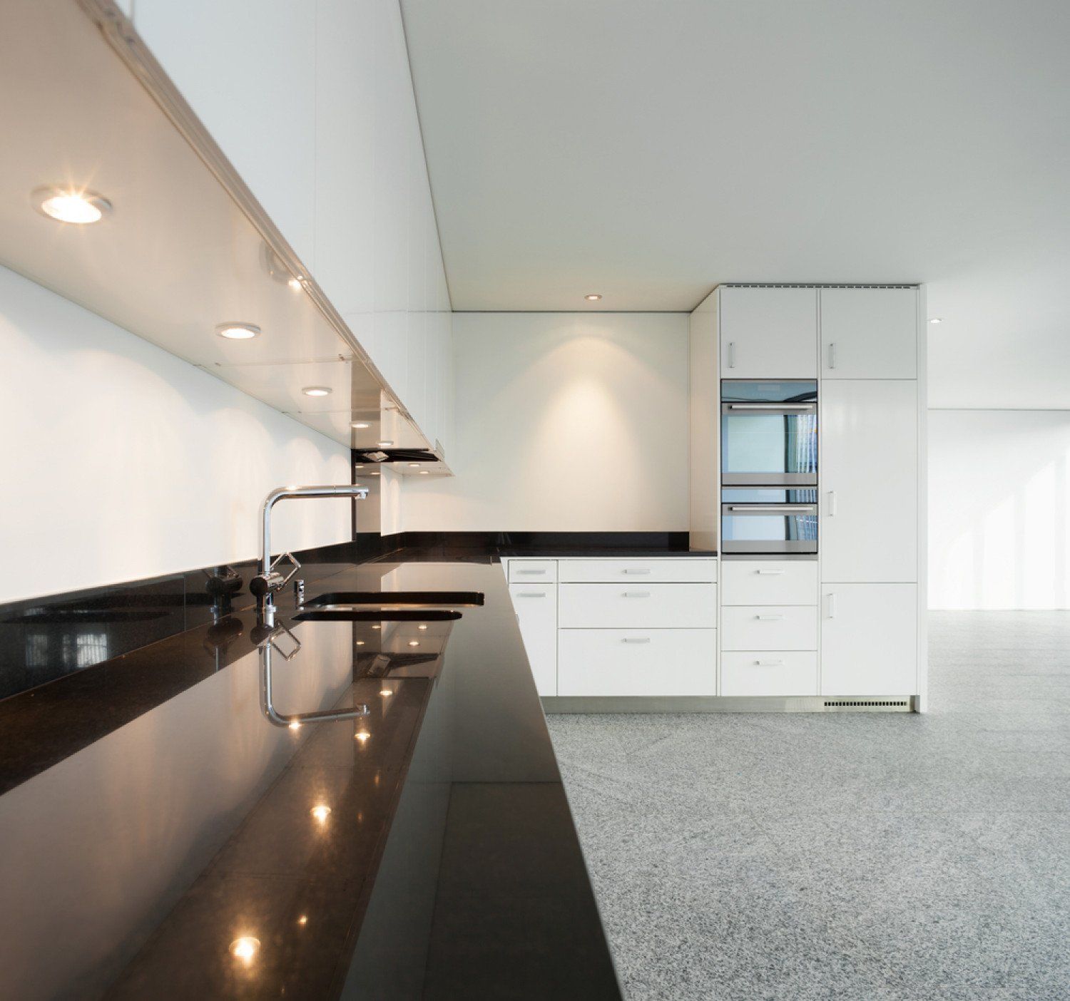 Modern white kitchen with black countertops, glossy cabinets, and built-in appliances