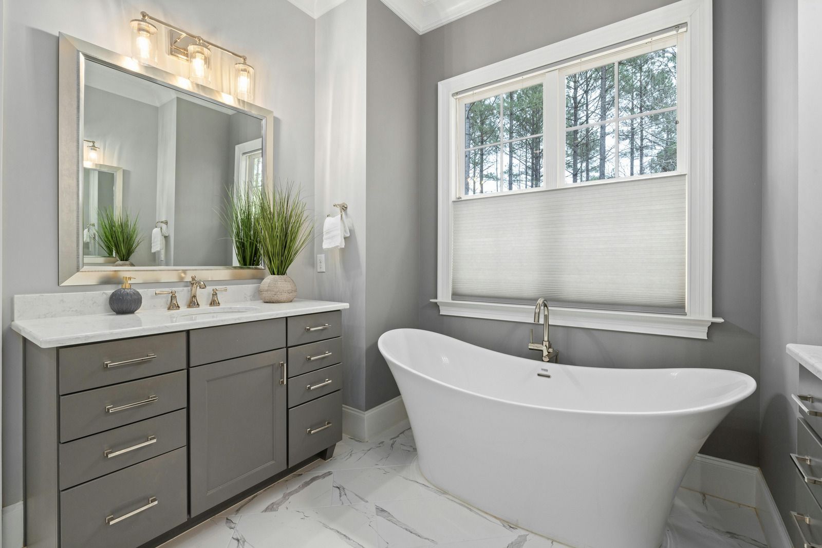 Modern gray bathroom with double vanity, large mirror, and a freestanding white tub by the window