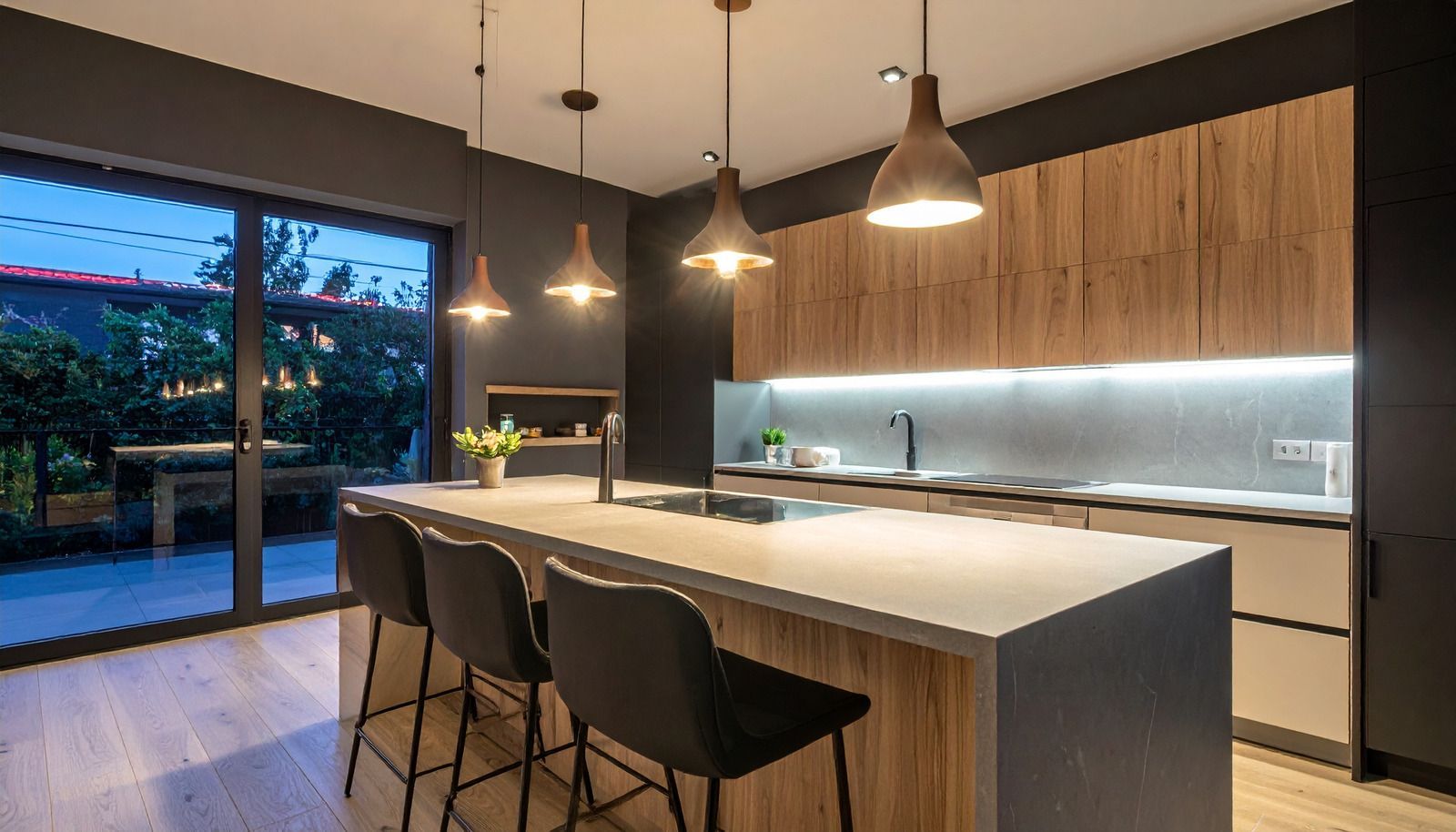 Modern kitchen with wood cabinets, island seating, pendant lights, and a glass door to the patio at dusk