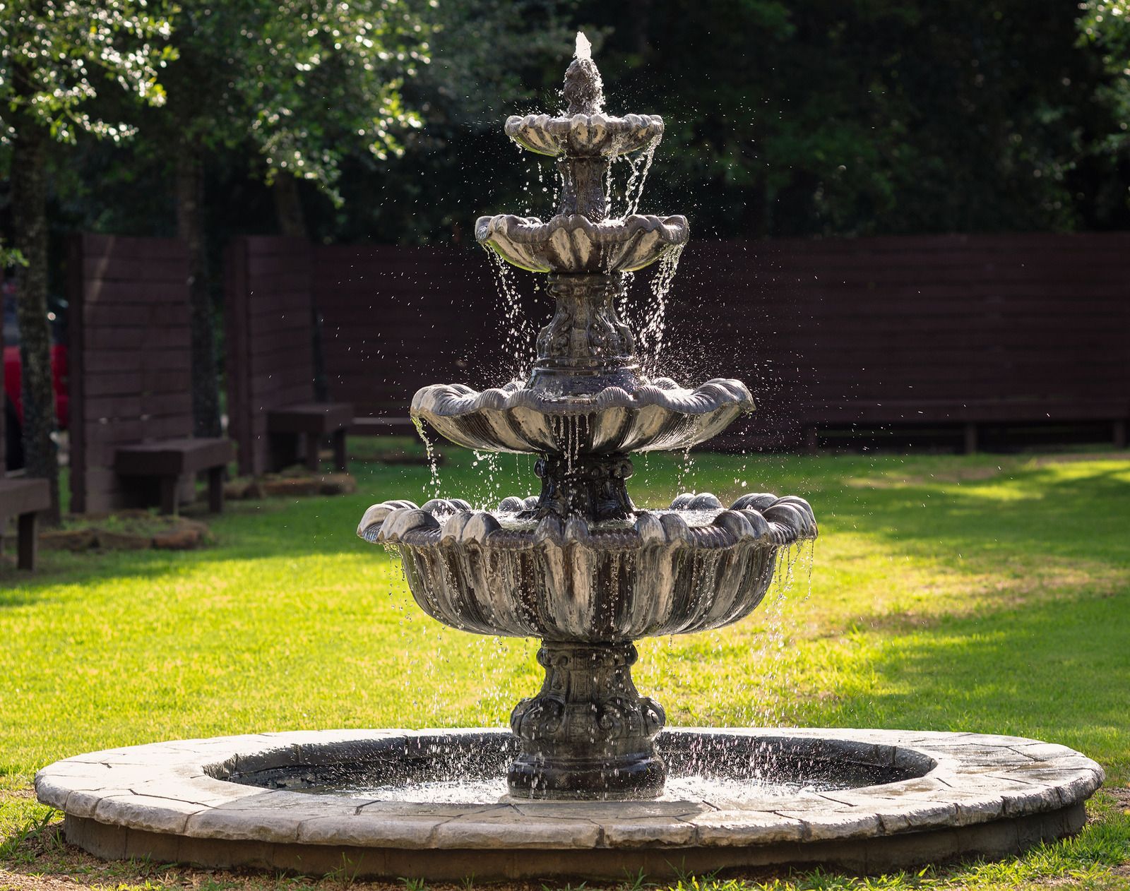 Stone fountain with water spraying in a sunny garden lawn
