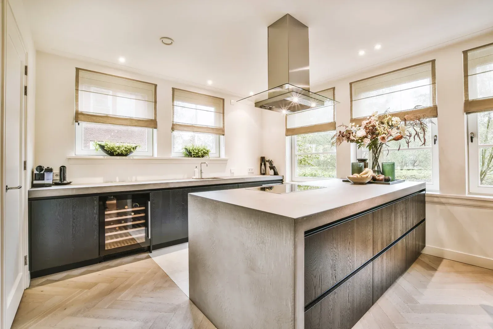 Bright modern kitchen with a large island, dark cabinets, and sunlit windows