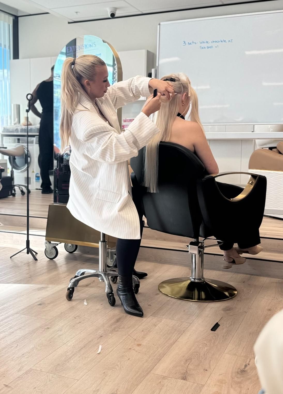 Woman in Lab Coat Styling Another Woman's Blonde Hair in a Classroom — Gina T Hair & Beauty In Mackay, QLD