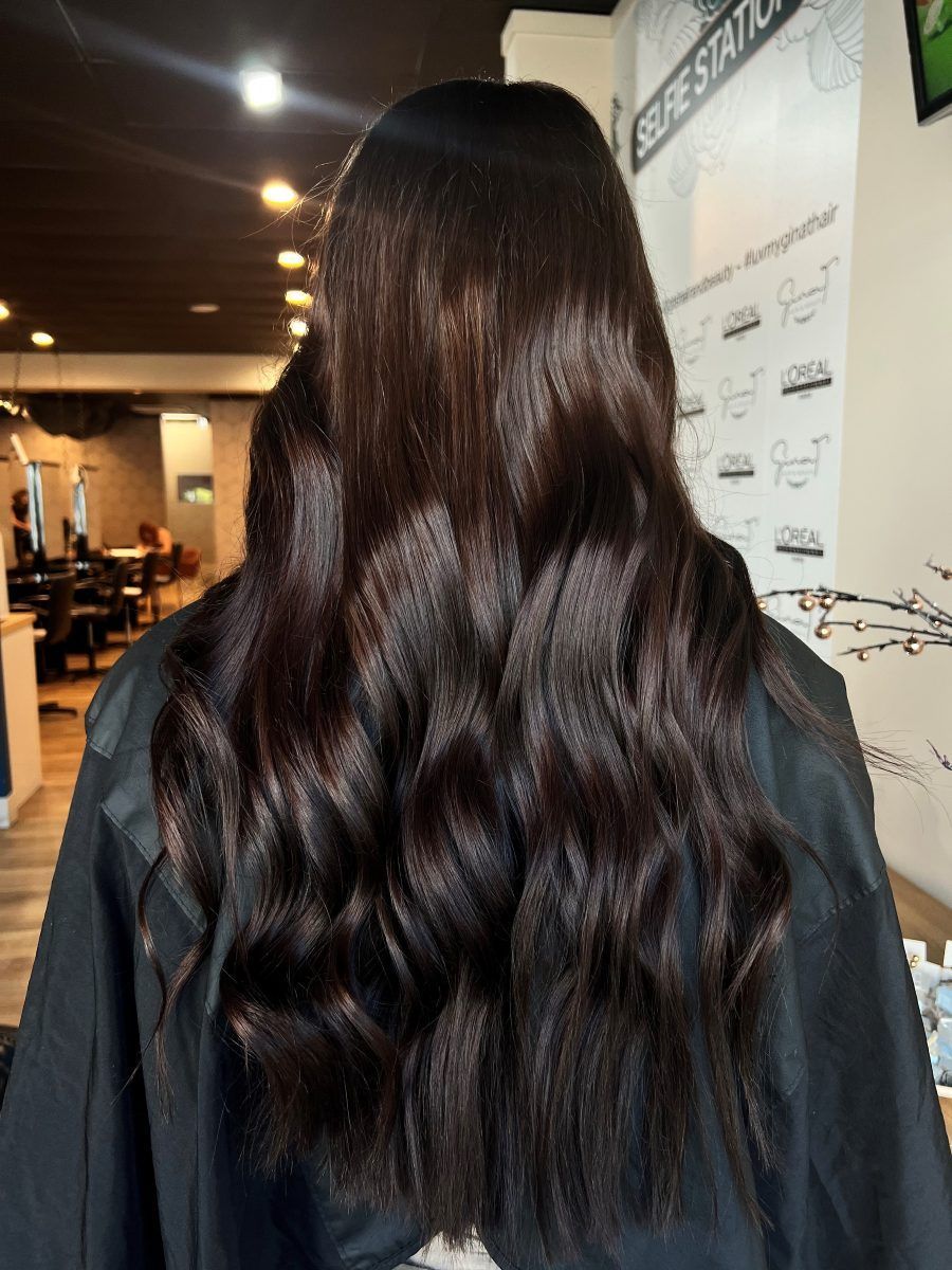 A Person With Long, Dark Brown Wavy Hair, Seated In A Salon — Gina T Hair & Beauty In Mackay, QLD