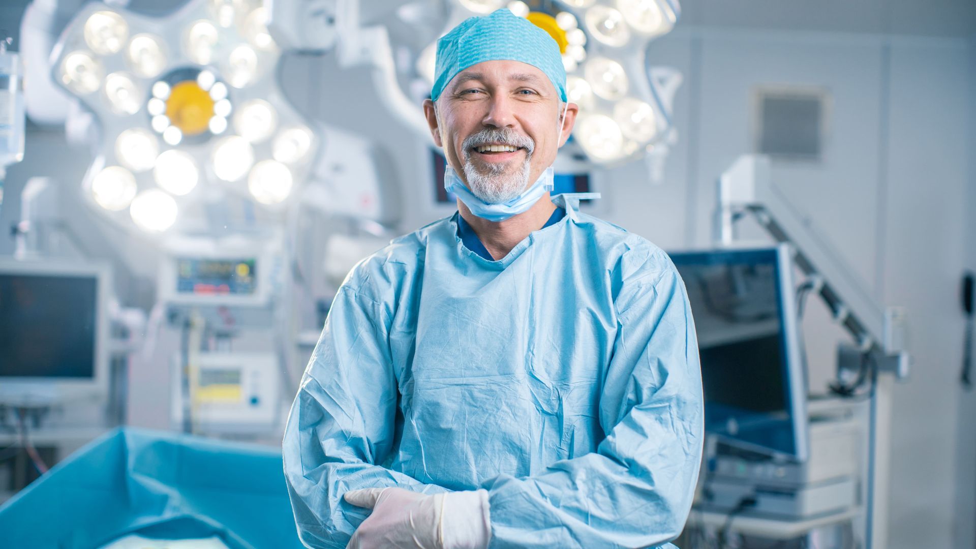 Um cirurgião está de pé em uma sala de cirurgia com os braços cruzados.