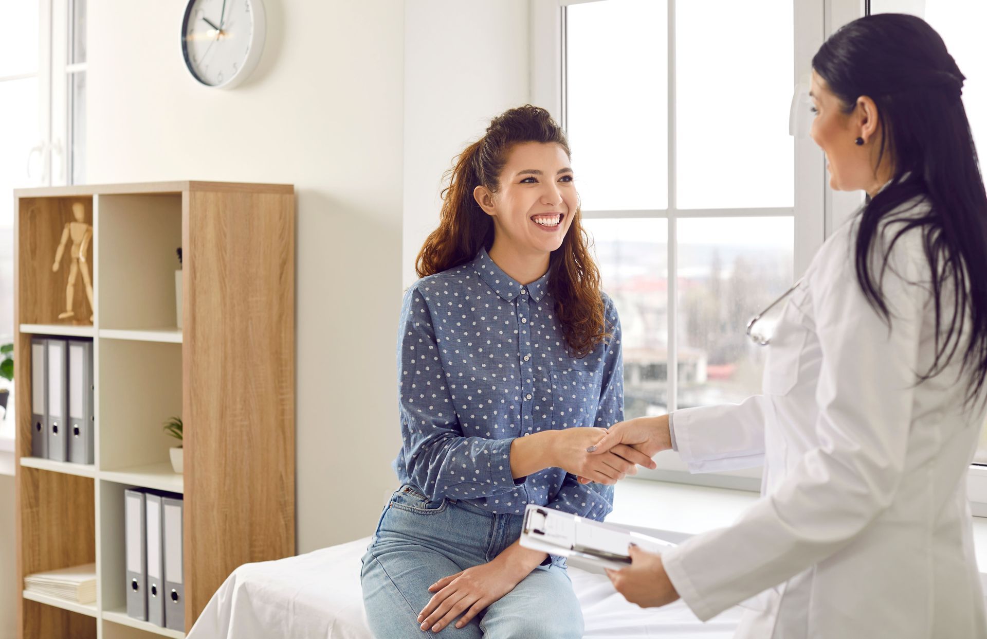 Uma mulher está sentada na cama apertando a mão de um médico.