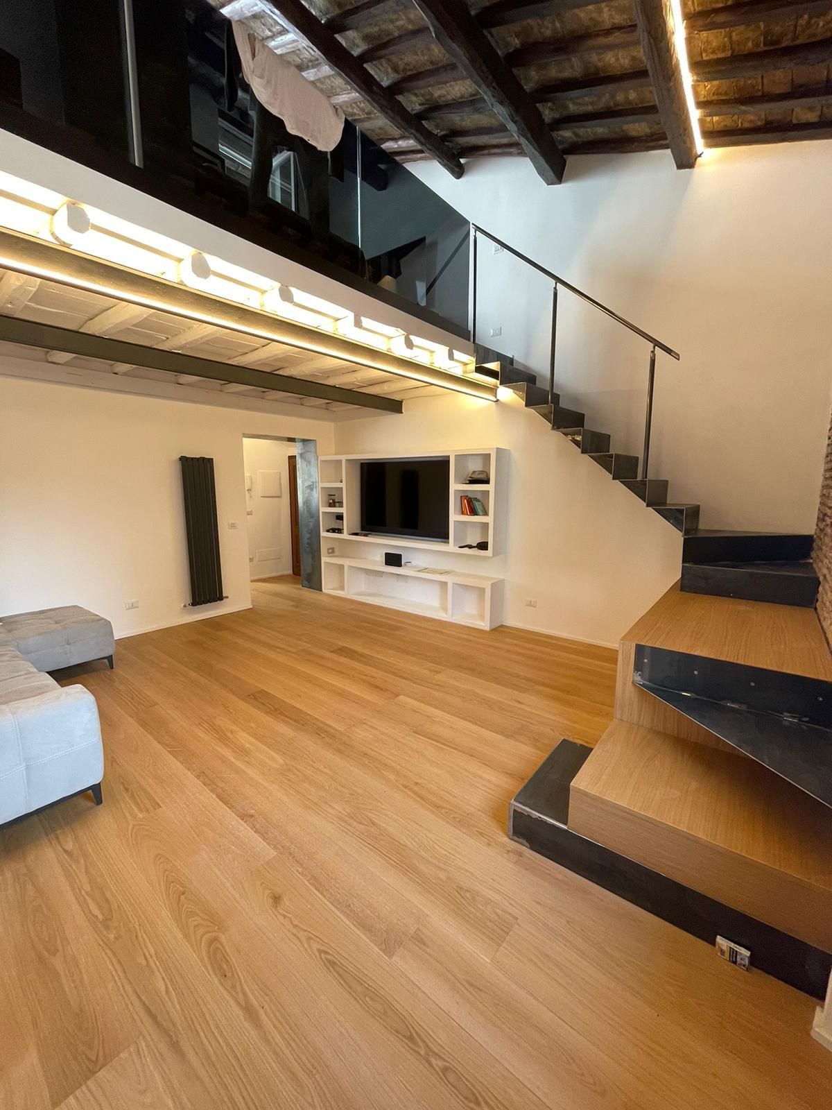Luminoso soggiorno con pavimenti in legno, centro di intrattenimento integrato e una scala che conduce a un soppalco.