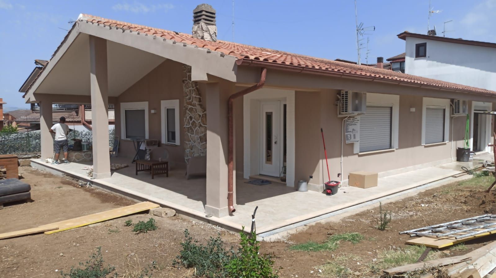 Casa color marrone chiaro con veranda coperta, tetto in tegole rosse e un operaio.