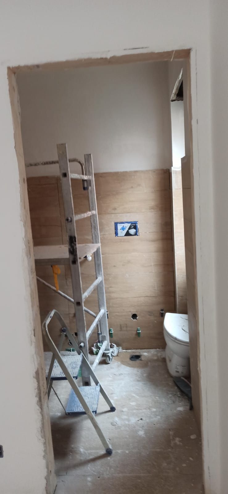 Un bagno in costruzione con una scala e un water visibili all'interno dello stipite della porta.