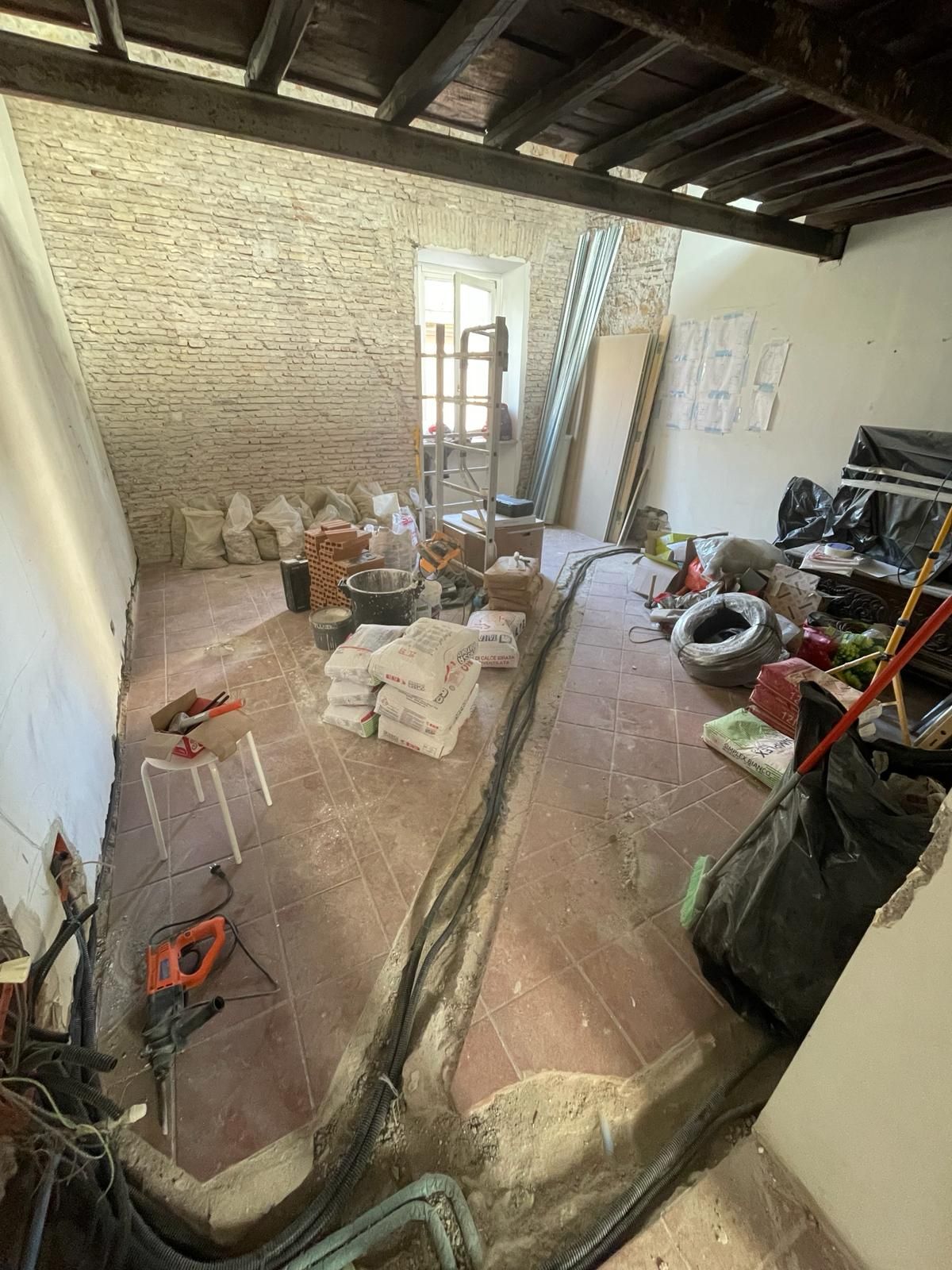 Ristrutturazione in corso: stanza interna con parete in mattoni a vista, materiali da costruzione e attrezzi sparsi sul pavimento.