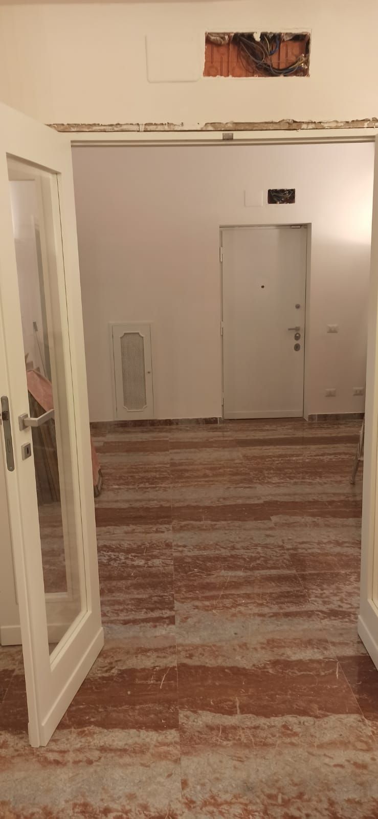 Una porta aperta conduce in una stanza con pavimenti in legno consumati e una porta bianca sul retro.
