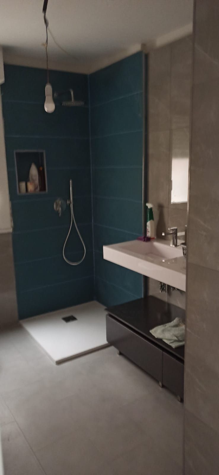Bagno moderno con doccia color verde acqua, piastrelle grigie e lavandino bianco sospeso.