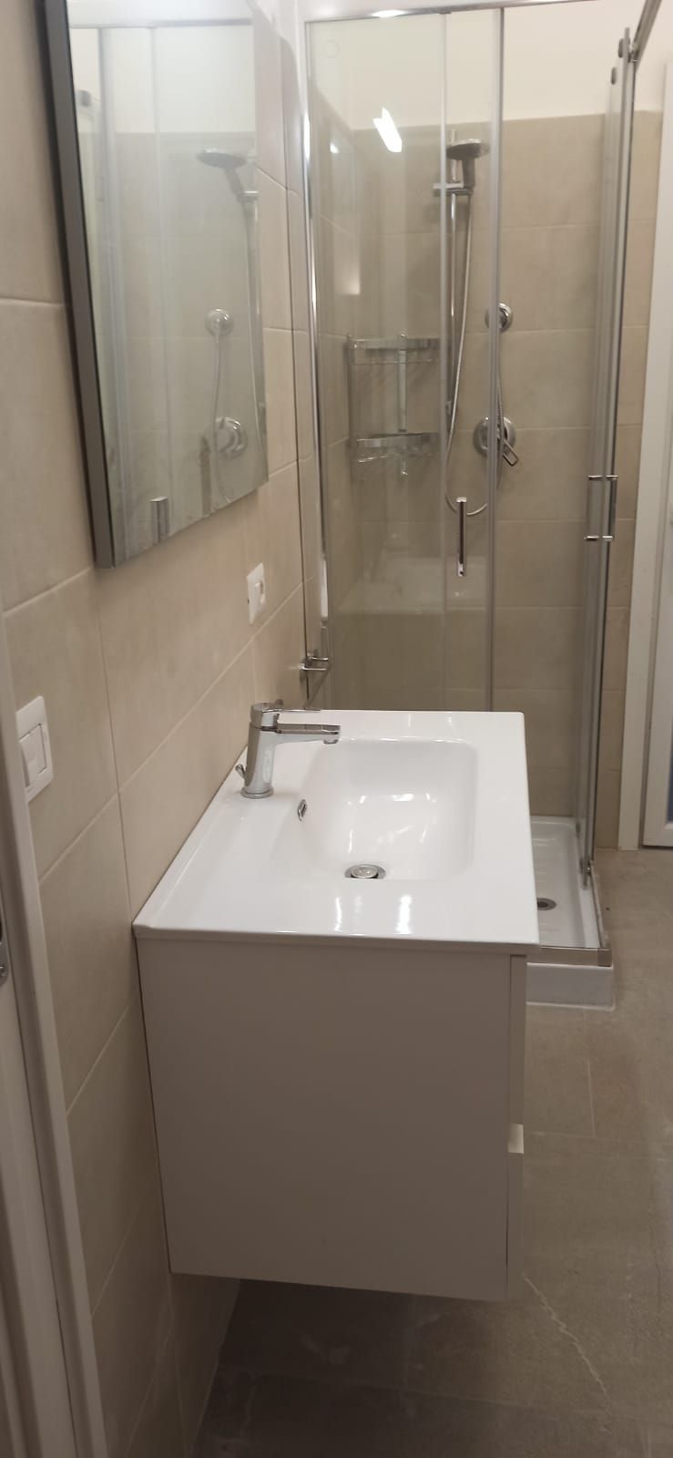 Bagno con lavandino bianco, specchio e box doccia in vetro.