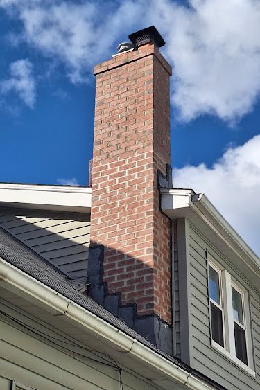 Brick chimney extending above a two-story house with dark shingles and blue sky.