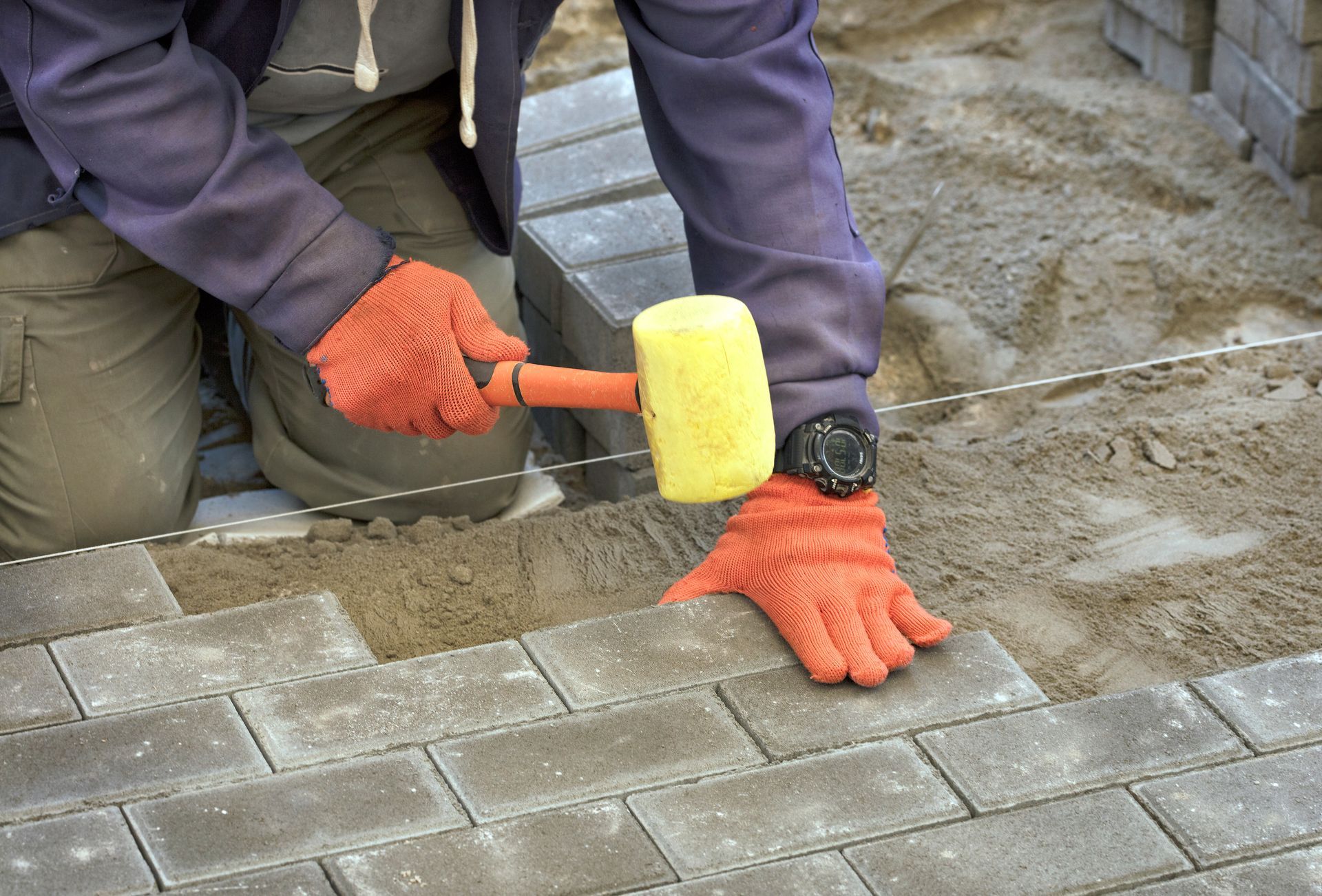 A masonry worker leveling paving stones with a rubber mallet.