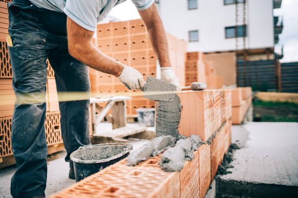 Worker applying mortar to bricks at construction site.