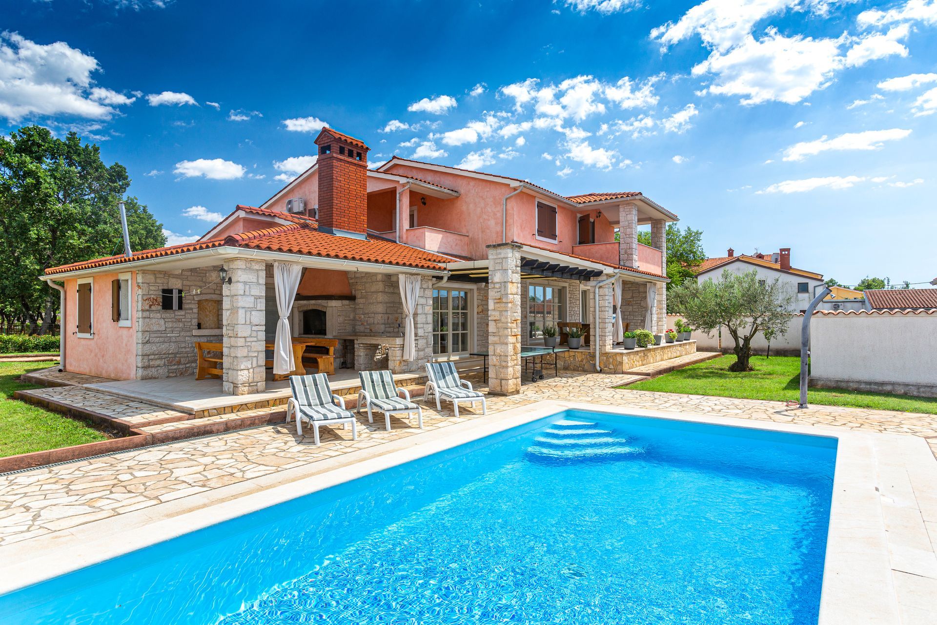 A house and a cottage with a pool surrounded by green foliage.