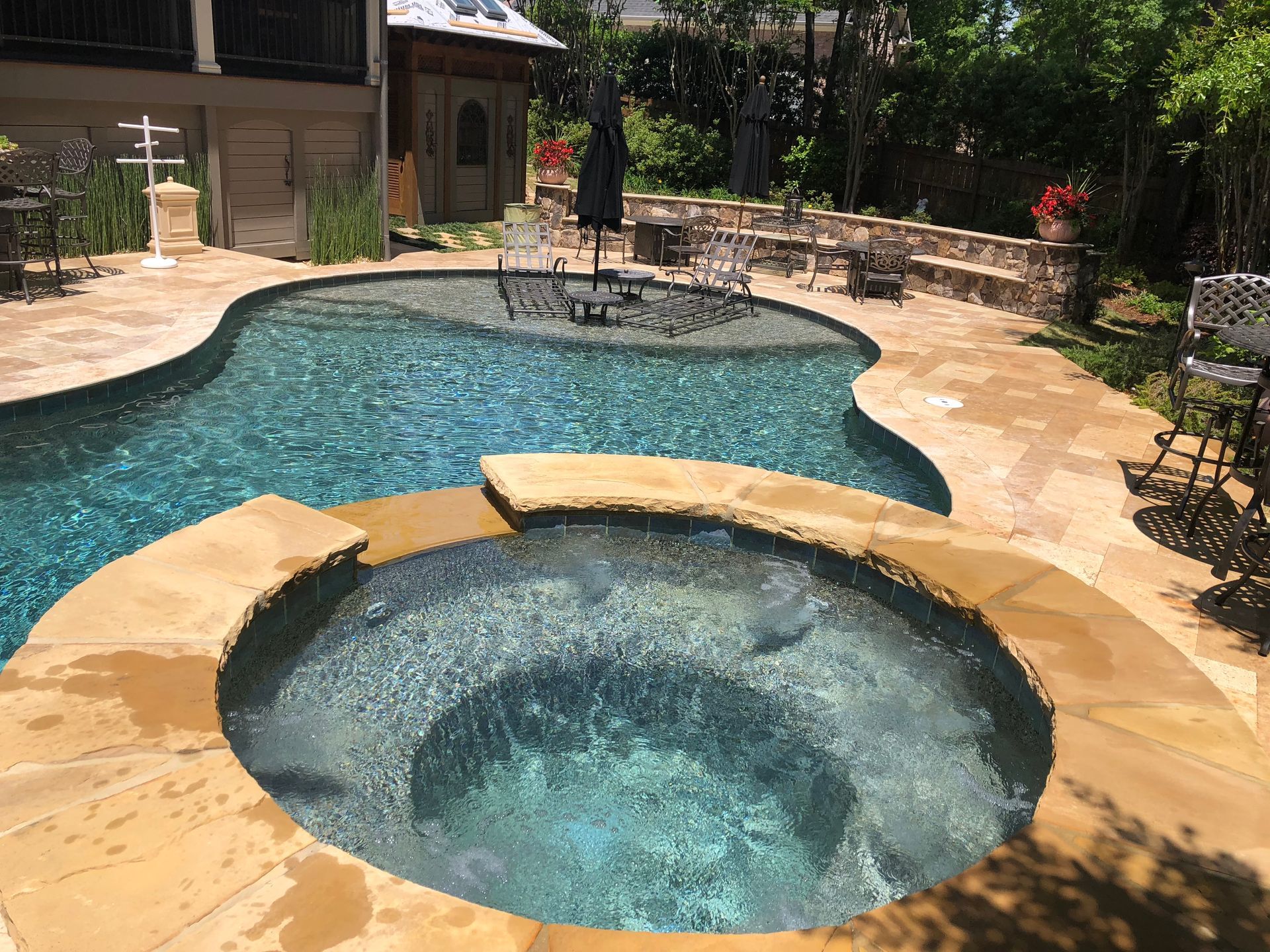 Pool and spa in a backyard with stone paving.